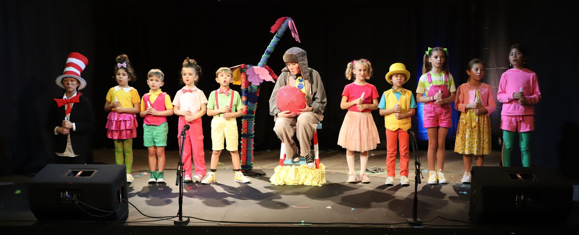 A group of children are standing on a stage in front of microphones.