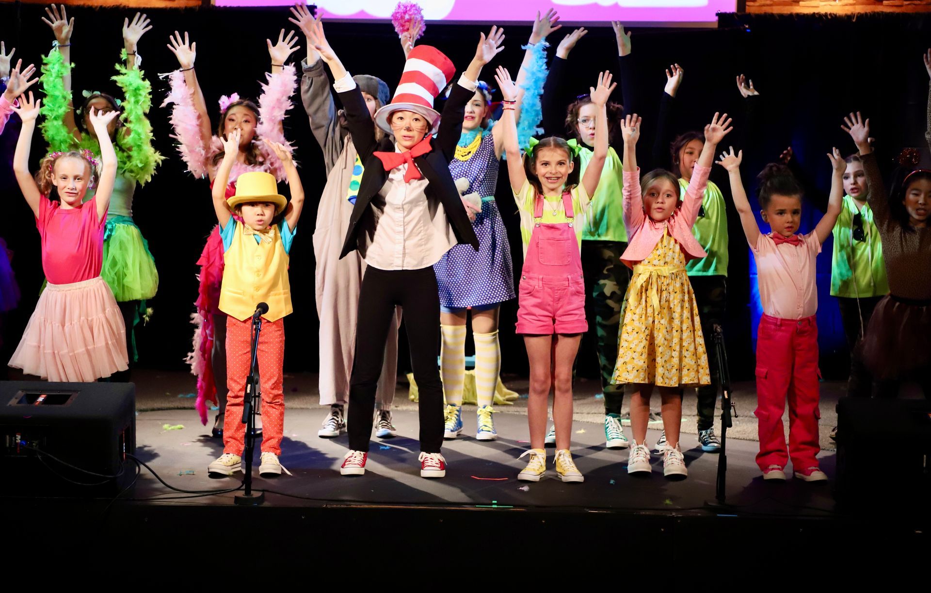 A group of children are standing on a stage with their hands in the air.