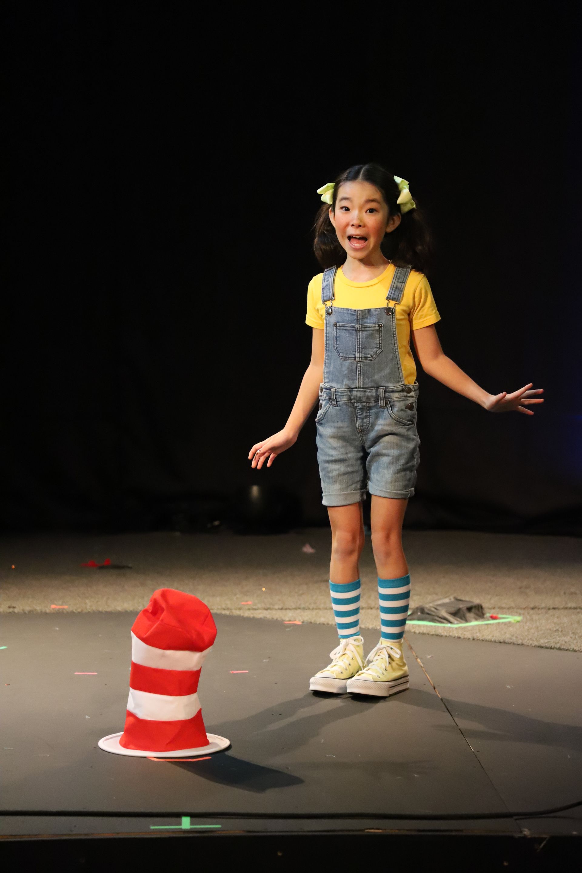 A little girl is standing next to a cat in the hat on a stage.