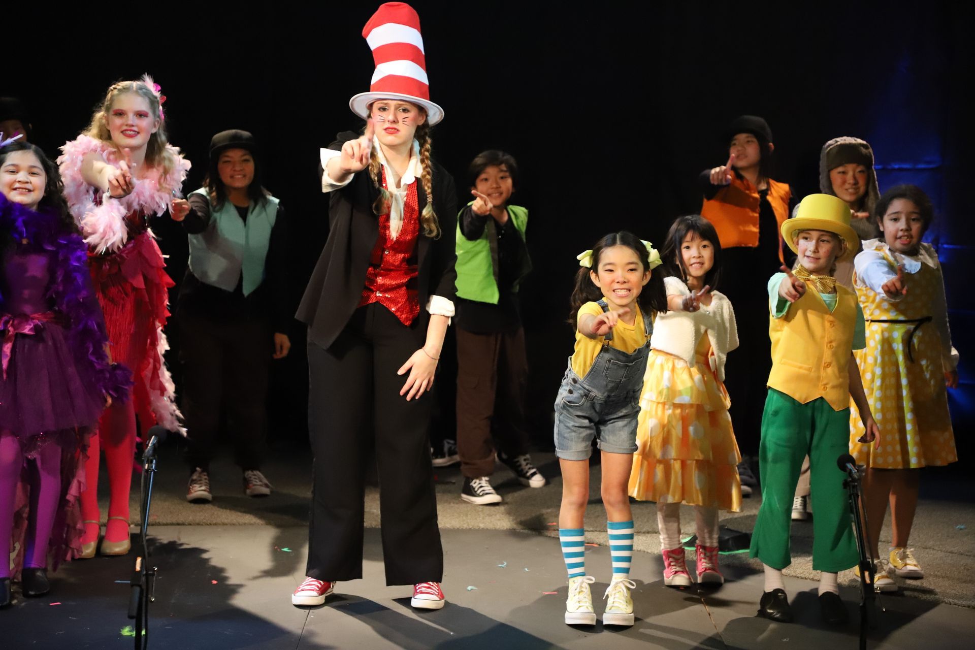 A woman in a cat in the hat is standing next to a group of children on a stage.