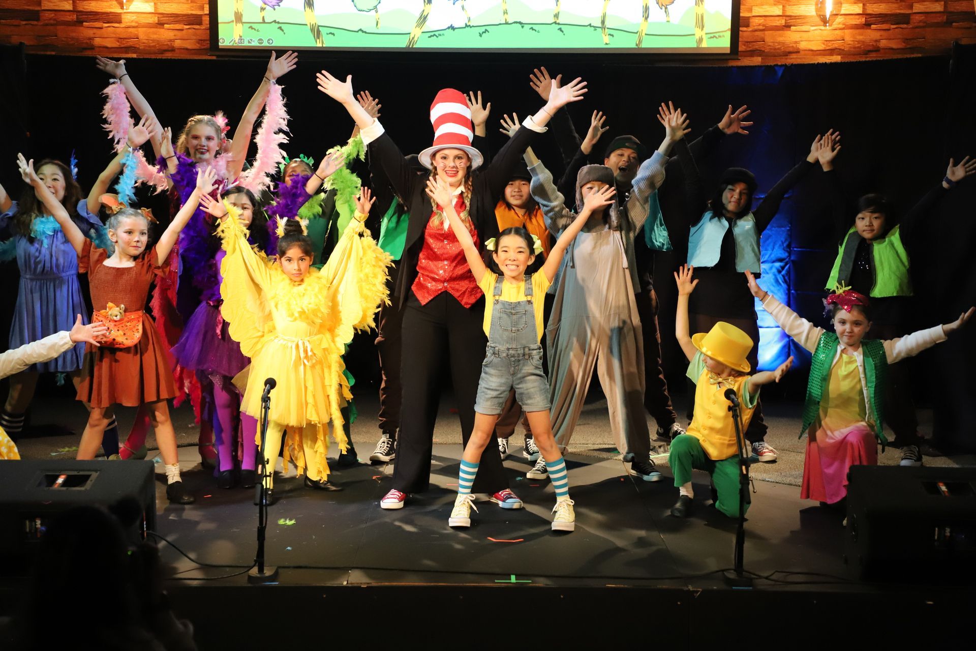 A group of children are standing on a stage with their arms in the air.