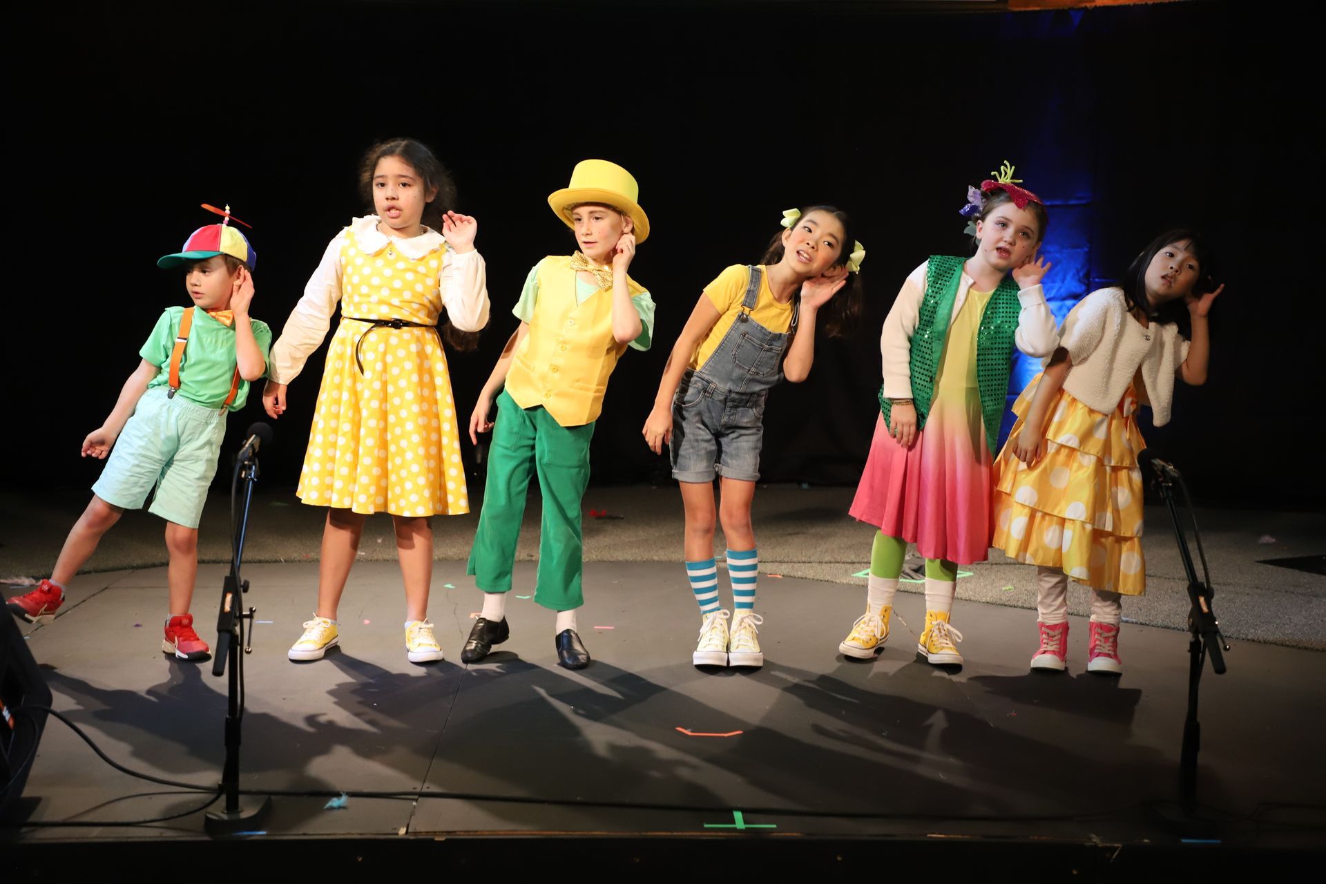 A group of children are standing on a stage in front of microphones.