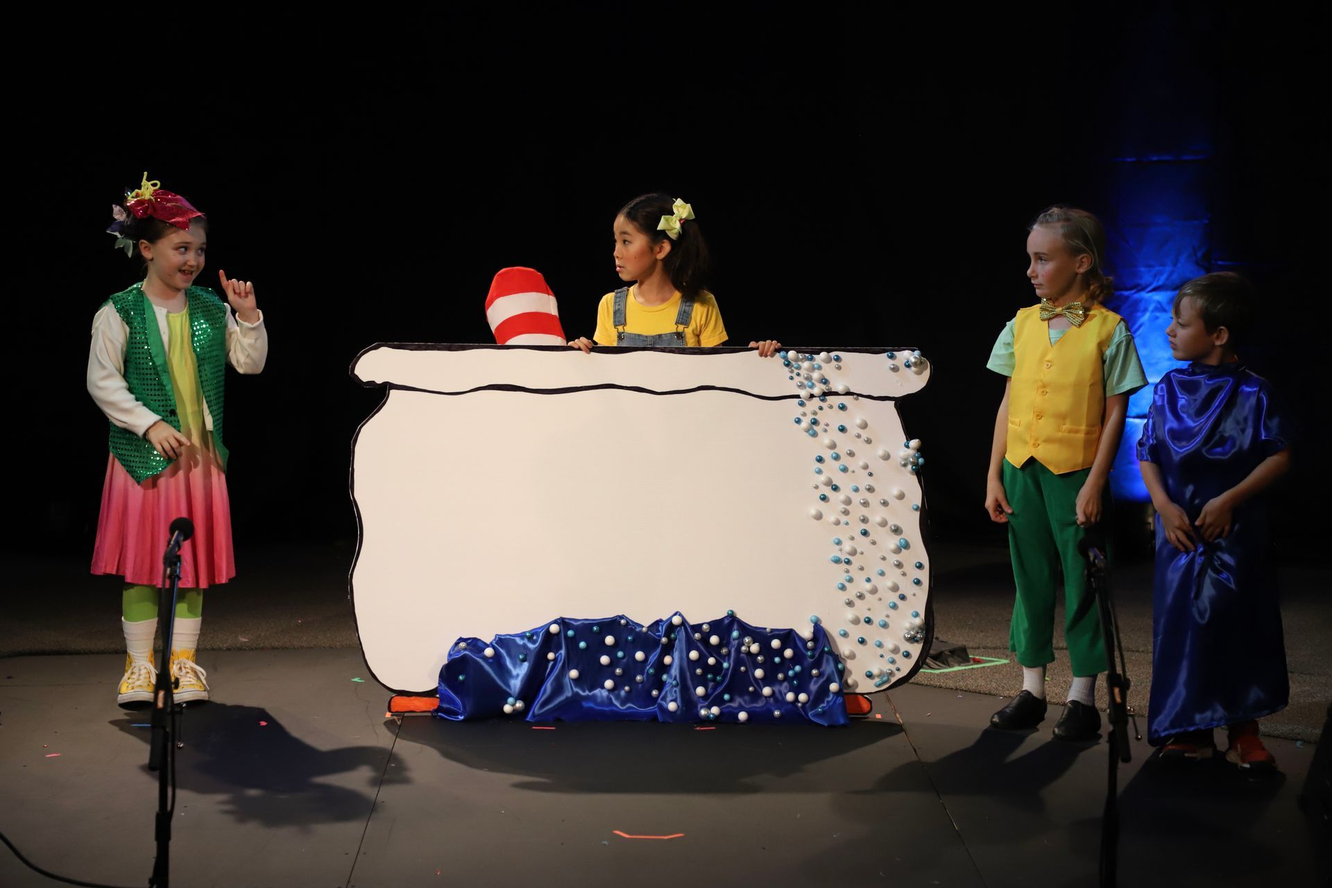 A group of children are standing on a stage in front of a cauldron.