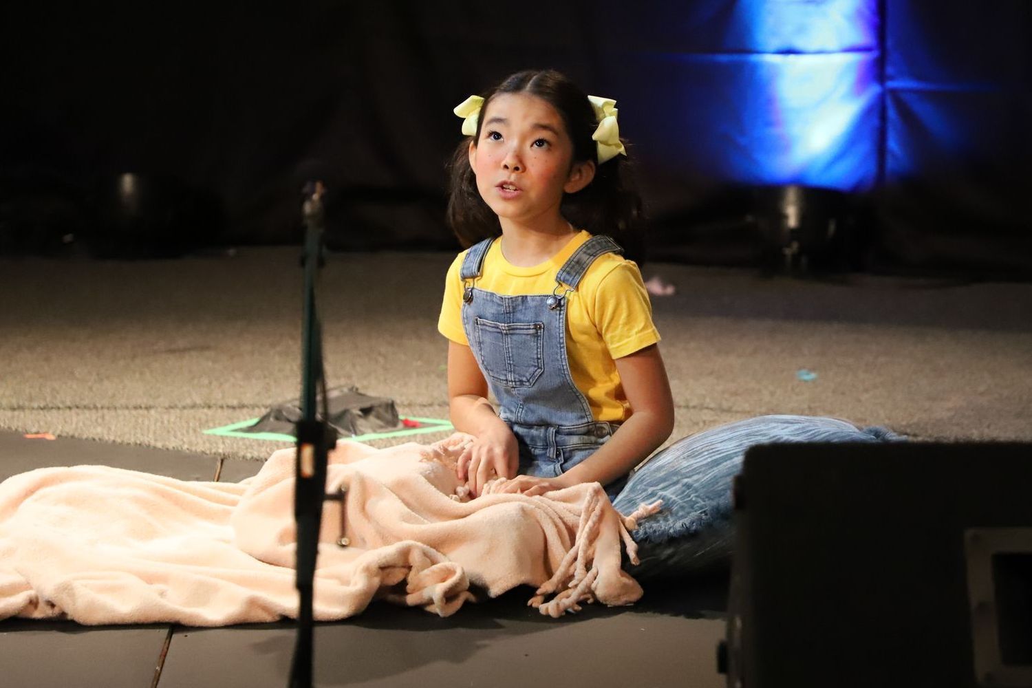 A little girl is sitting on the floor in front of a microphone.