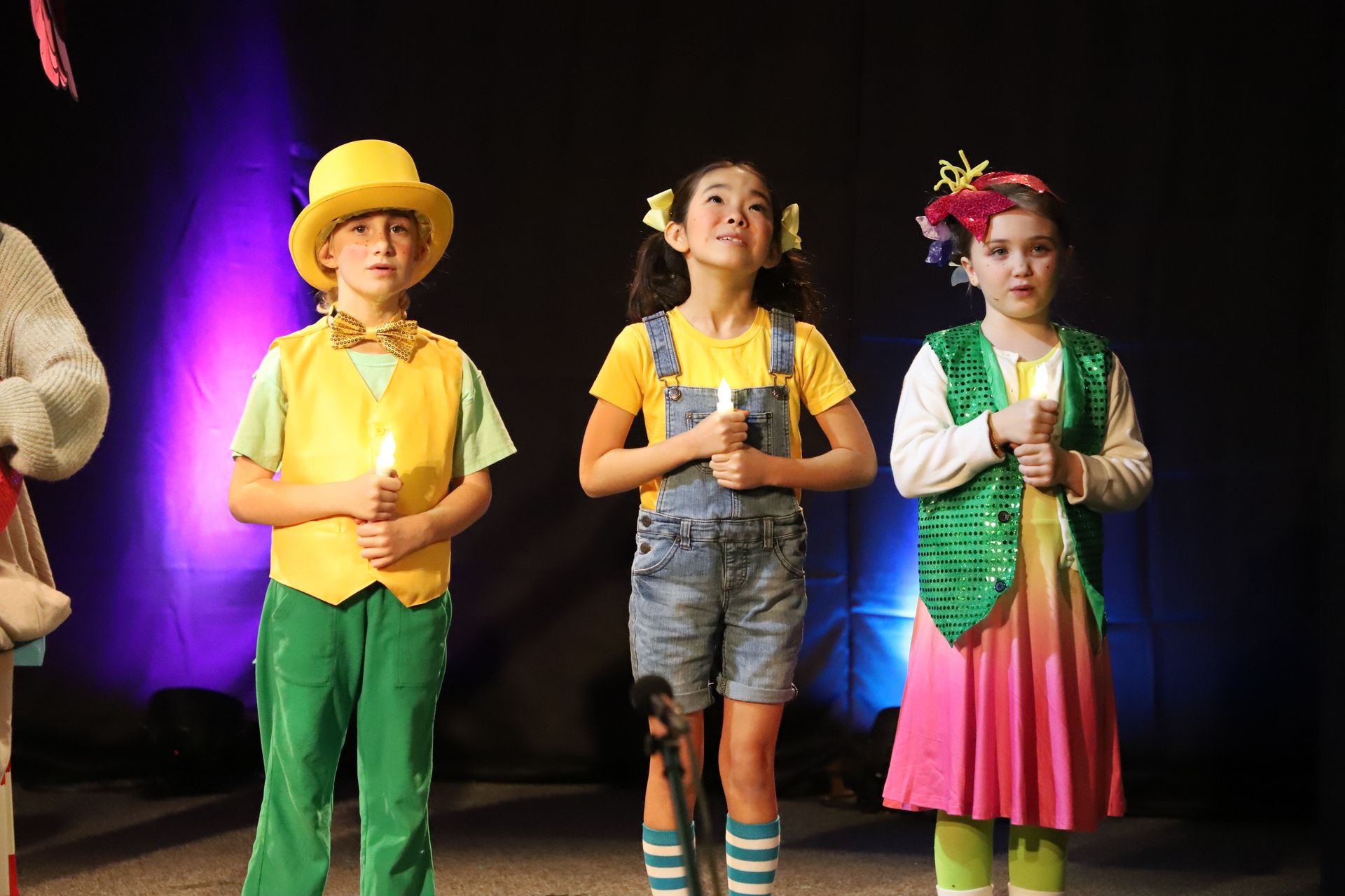 A group of children are standing on a stage holding candles.