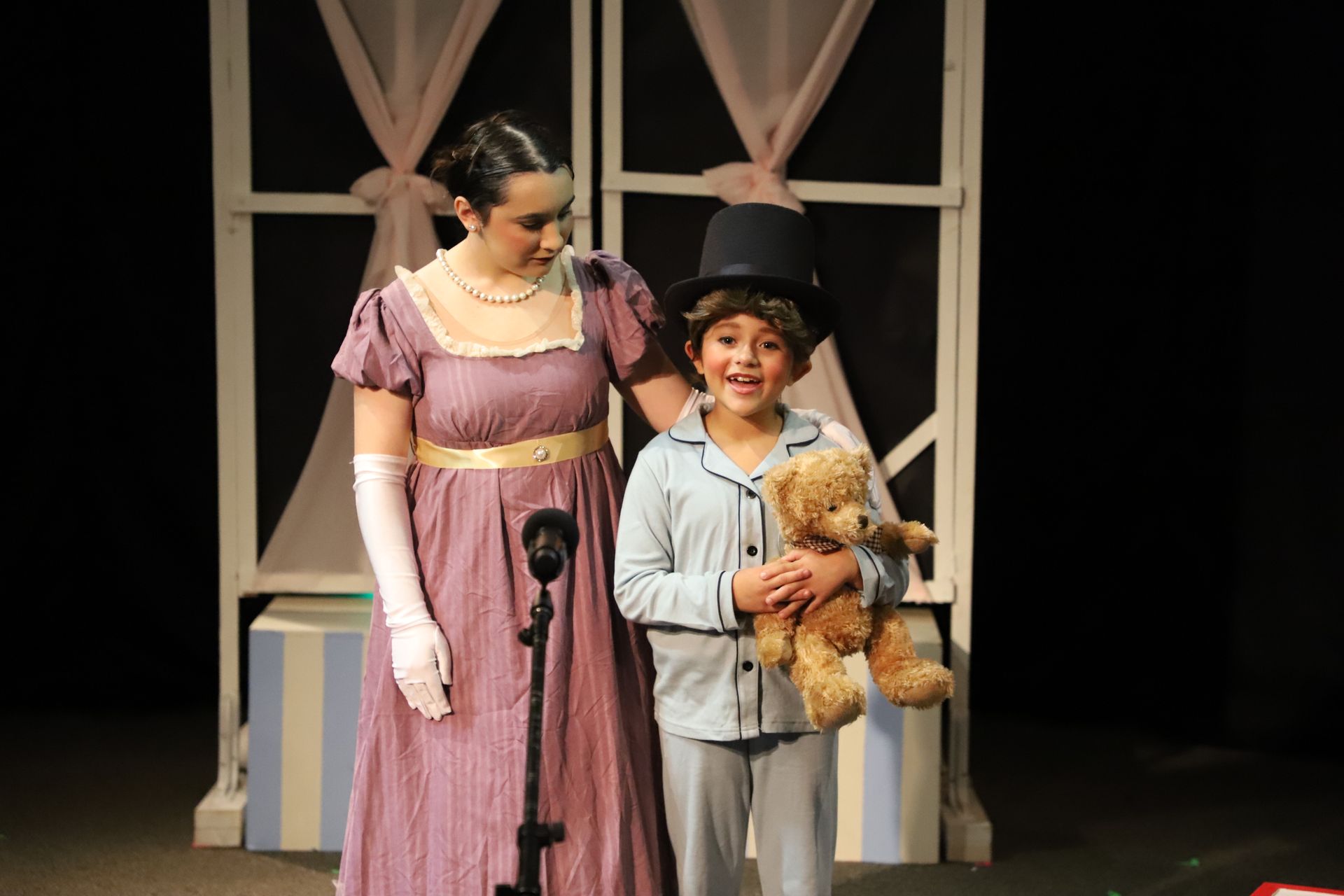 A woman in a top hat stands next to a boy holding a teddy bear