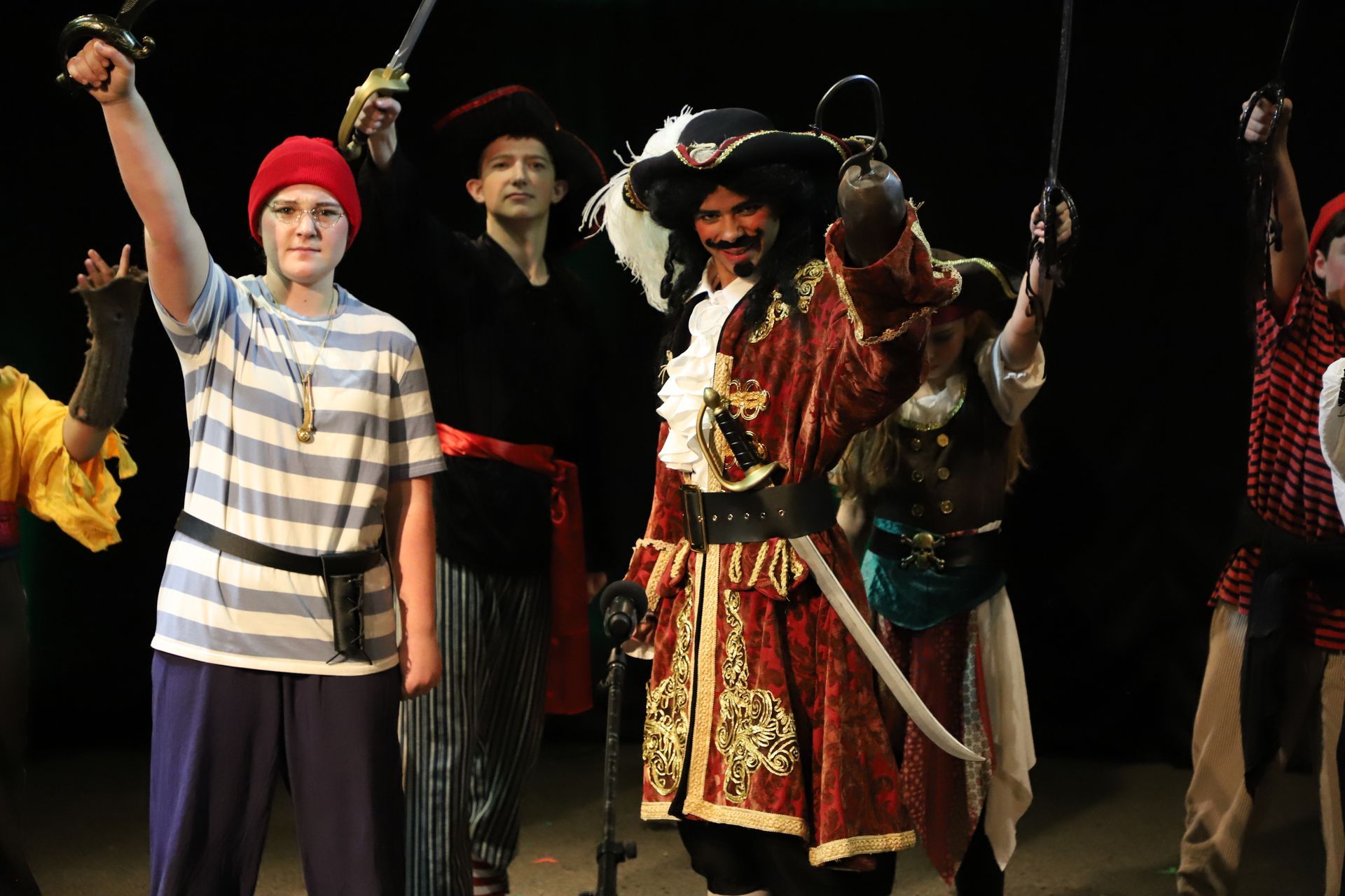 A group of people dressed as pirates are standing on a stage holding swords.