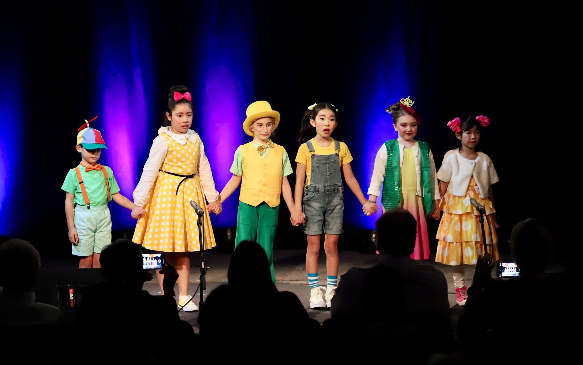 A group of children are holding hands on a stage.
