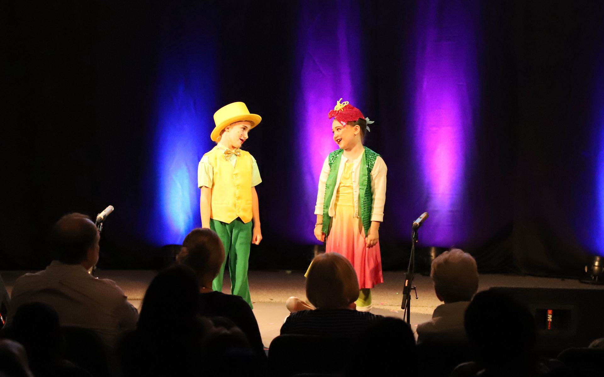 Two children are standing on a stage in front of a crowd.