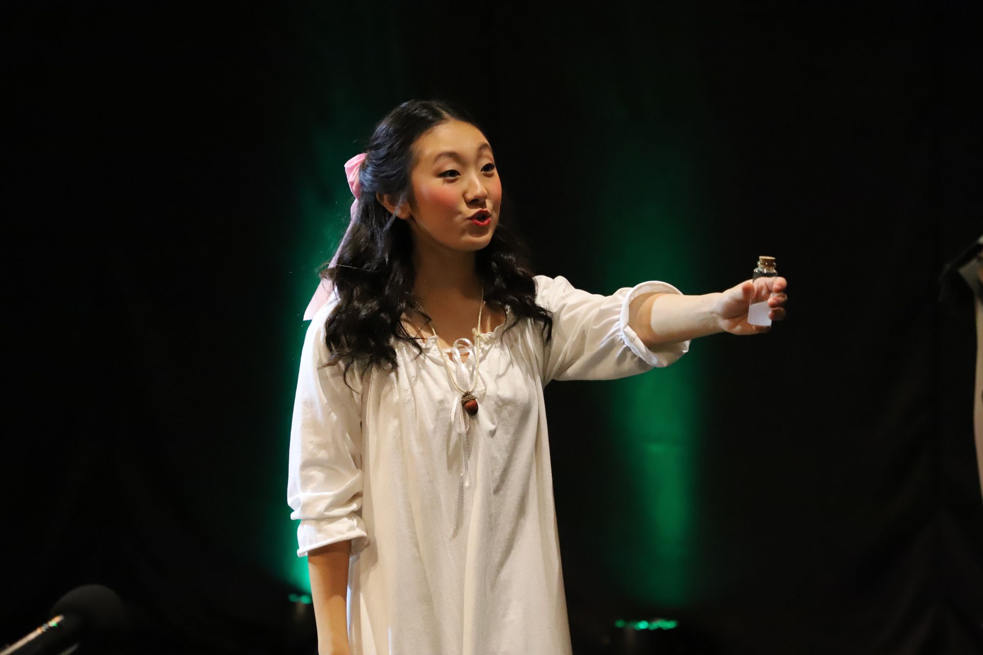 A woman in a white dress is standing on a stage holding a bottle.