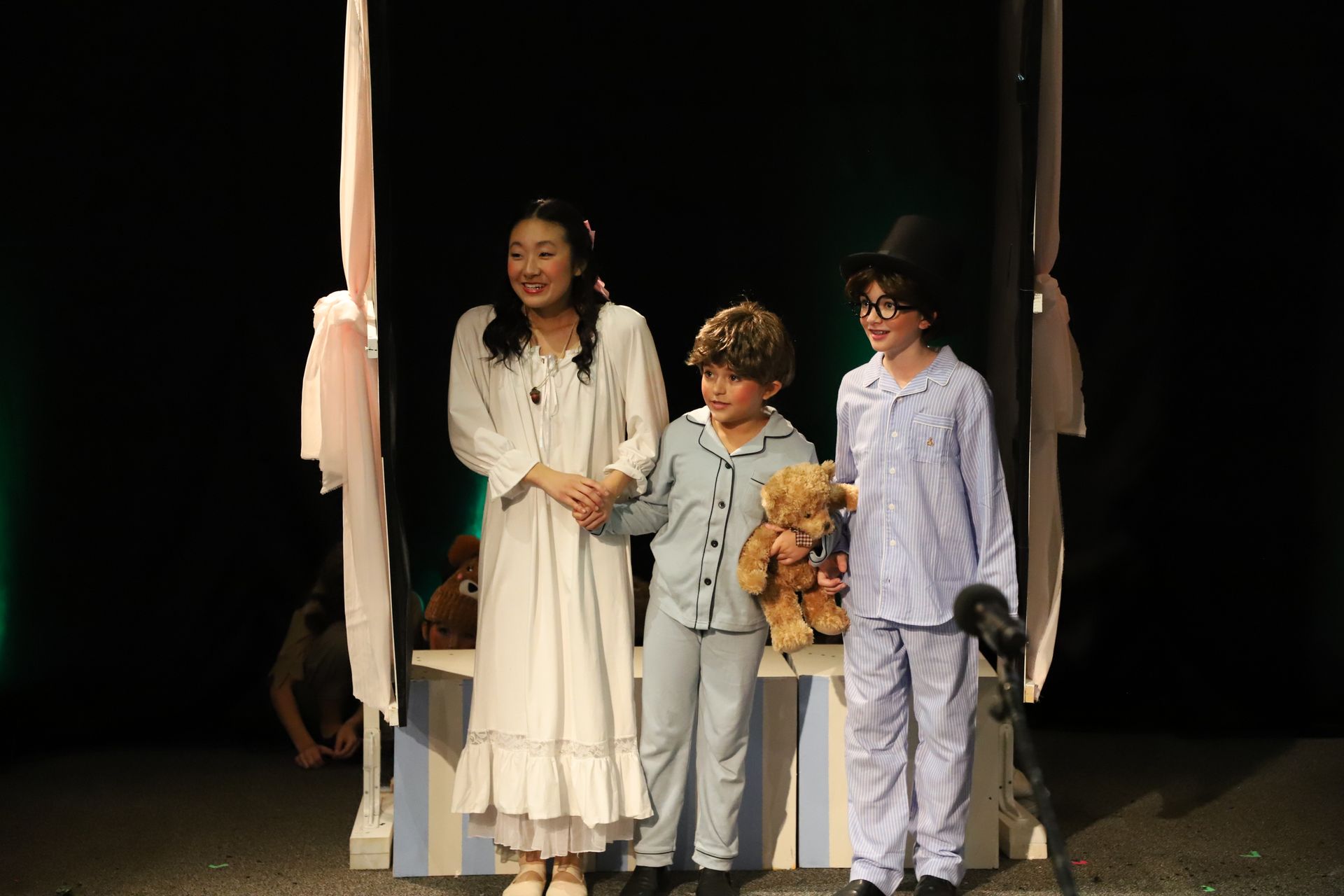 A group of children are standing on a stage holding teddy bears.