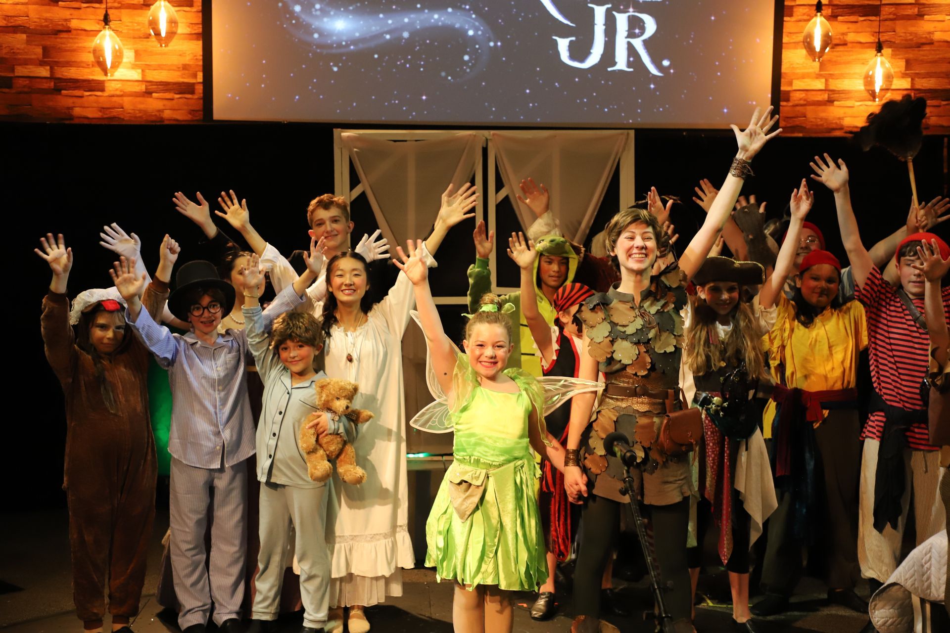 A group of children are standing on a stage with their hands in the air.