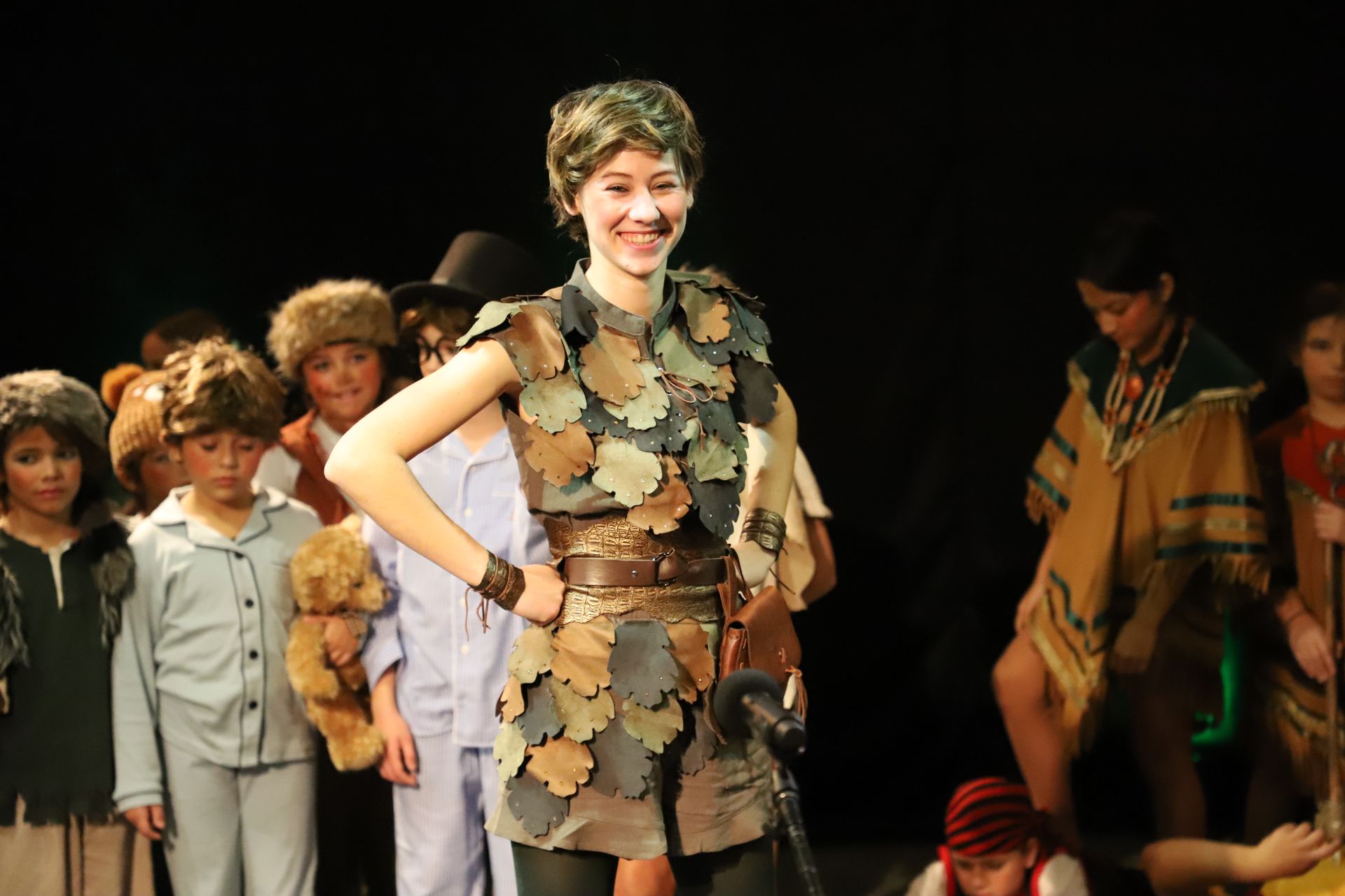 A girl in a peter pan costume is standing in front of a group of children