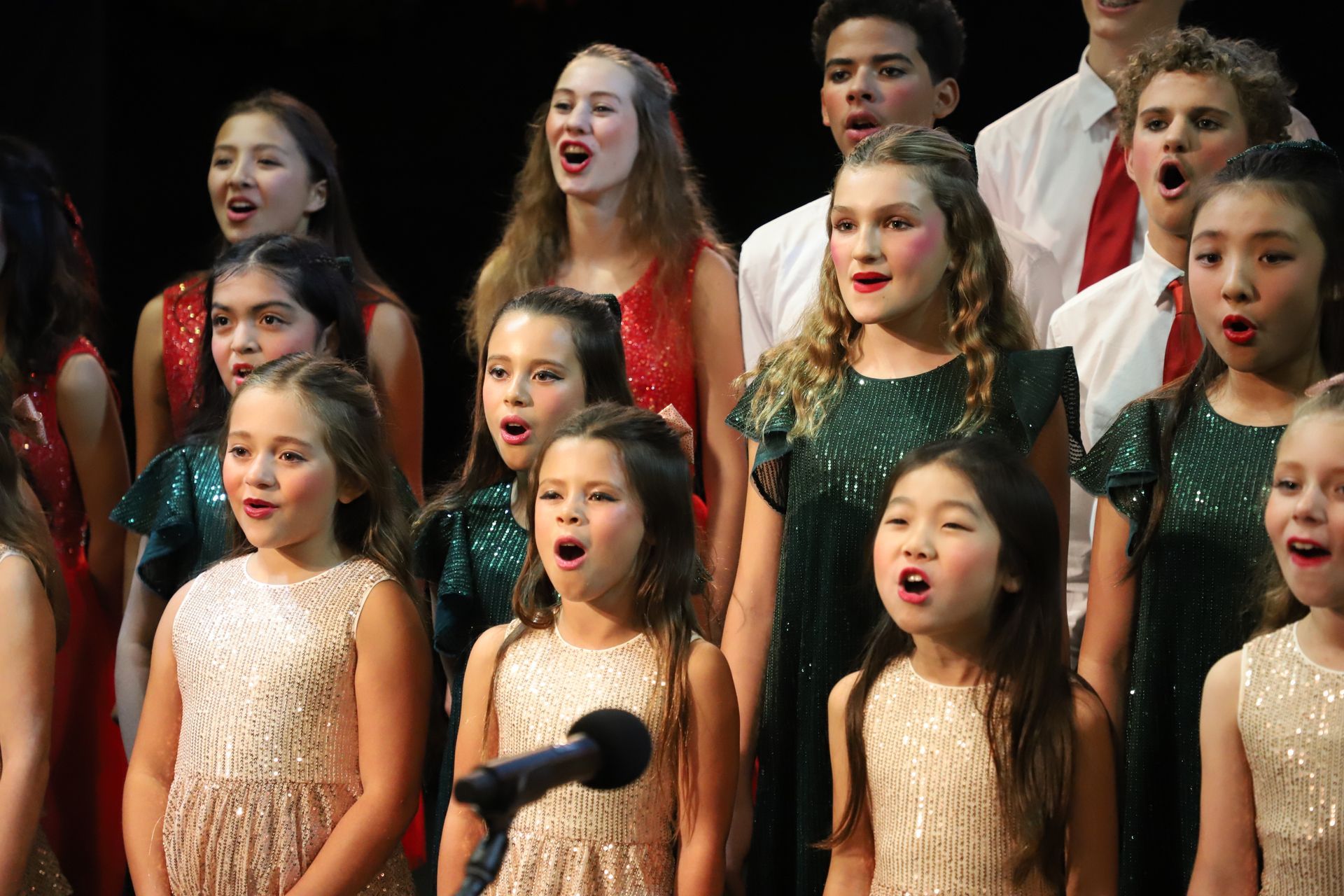 A group of young girls are singing into microphones in a choir.