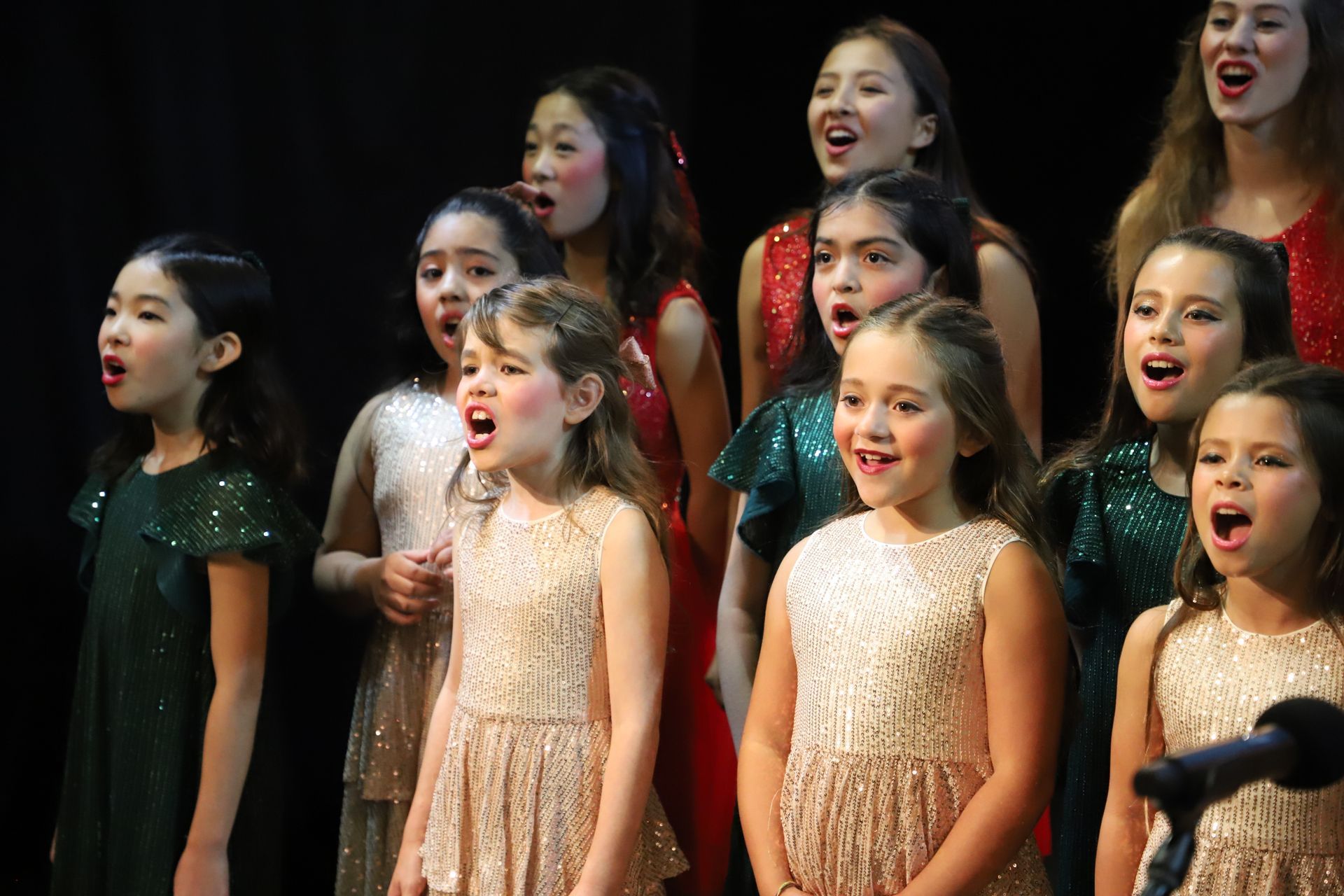 A group of young girls are singing in a choir on a stage.