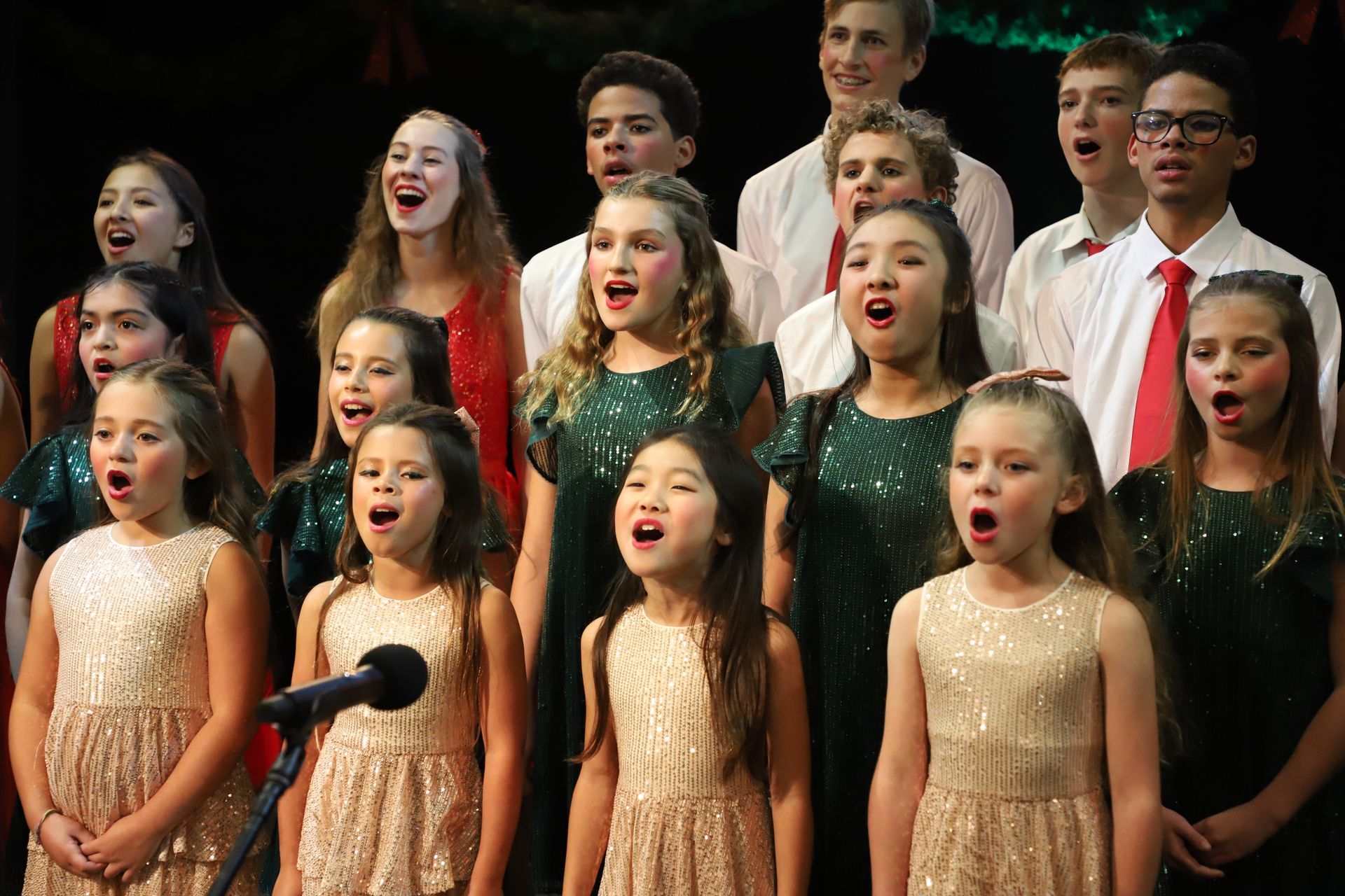 A group of children are singing into microphones in a choir.