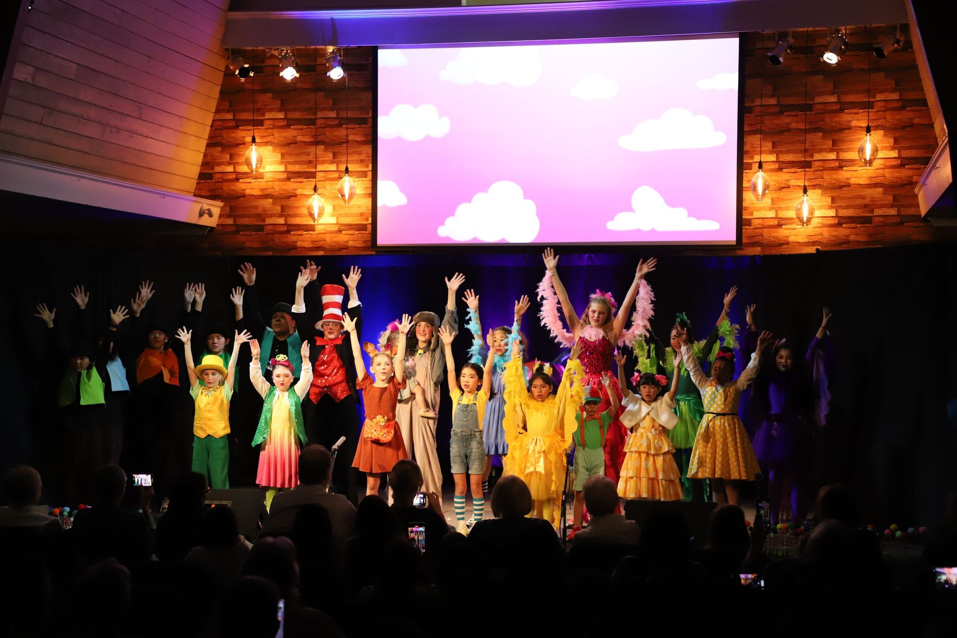 A group of children are standing on a stage with their hands in the air.