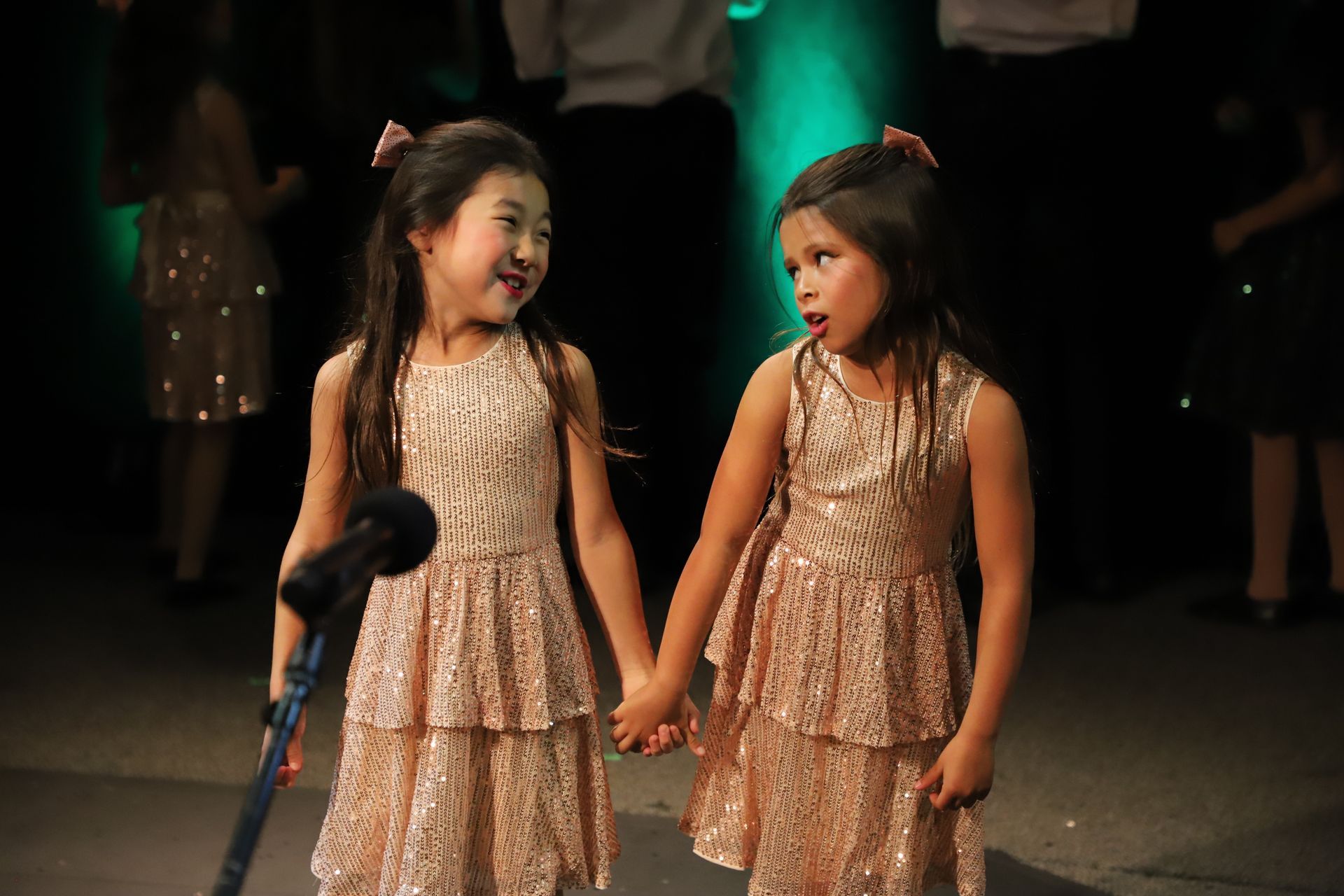 Two little girls are holding hands in front of a microphone.