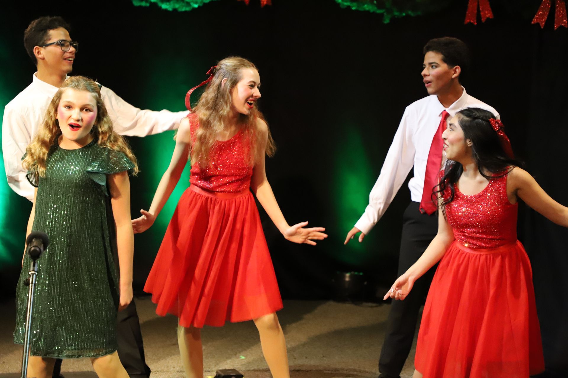 A group of young people in red dresses are dancing on a stage.