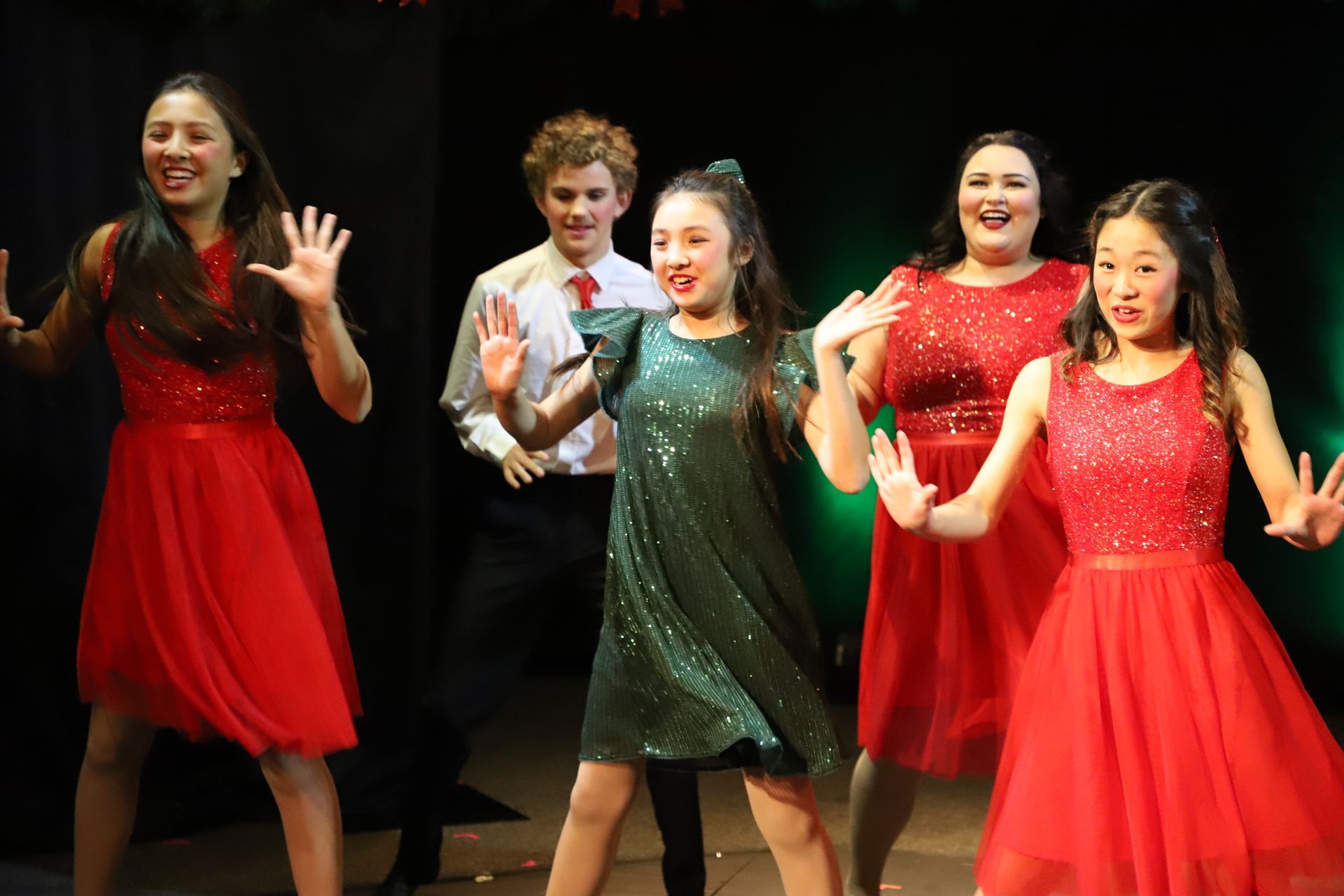 A group of young girls in red dresses are dancing on a stage.