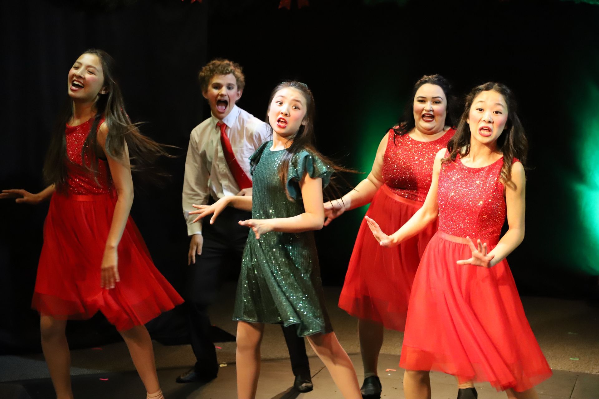 A group of young girls in red dresses are dancing on a stage.