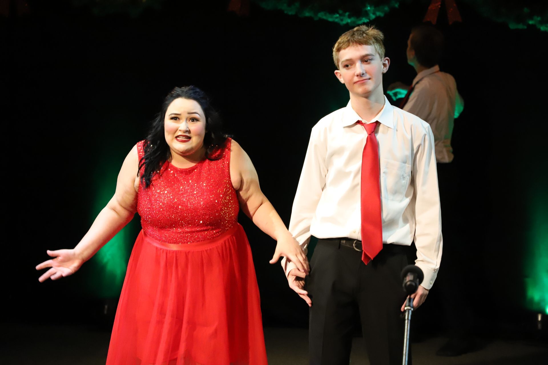 A man and a woman are standing next to each other on a stage holding hands.