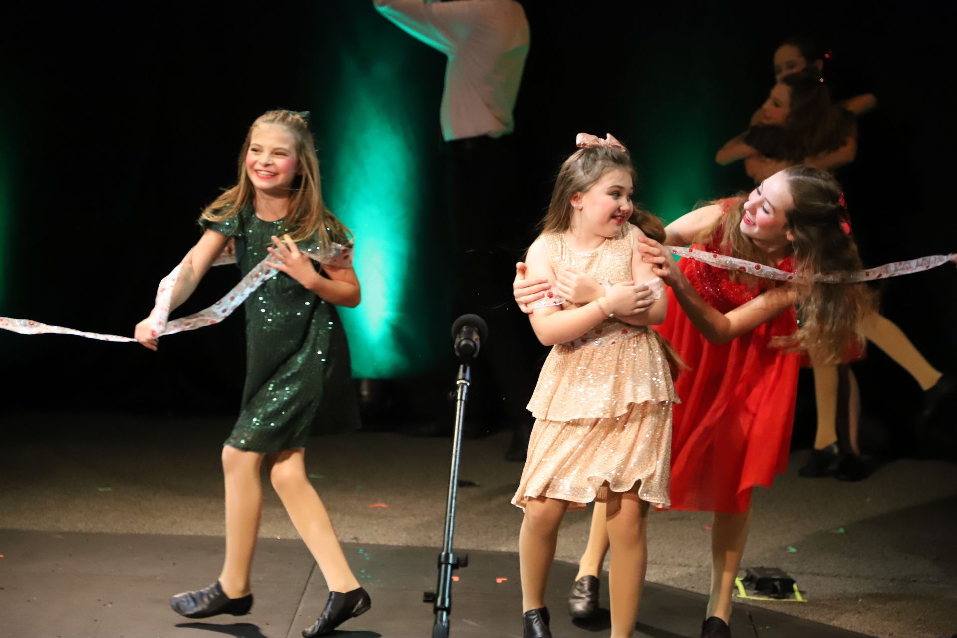 Three young girls are dancing on a stage in front of a microphone.