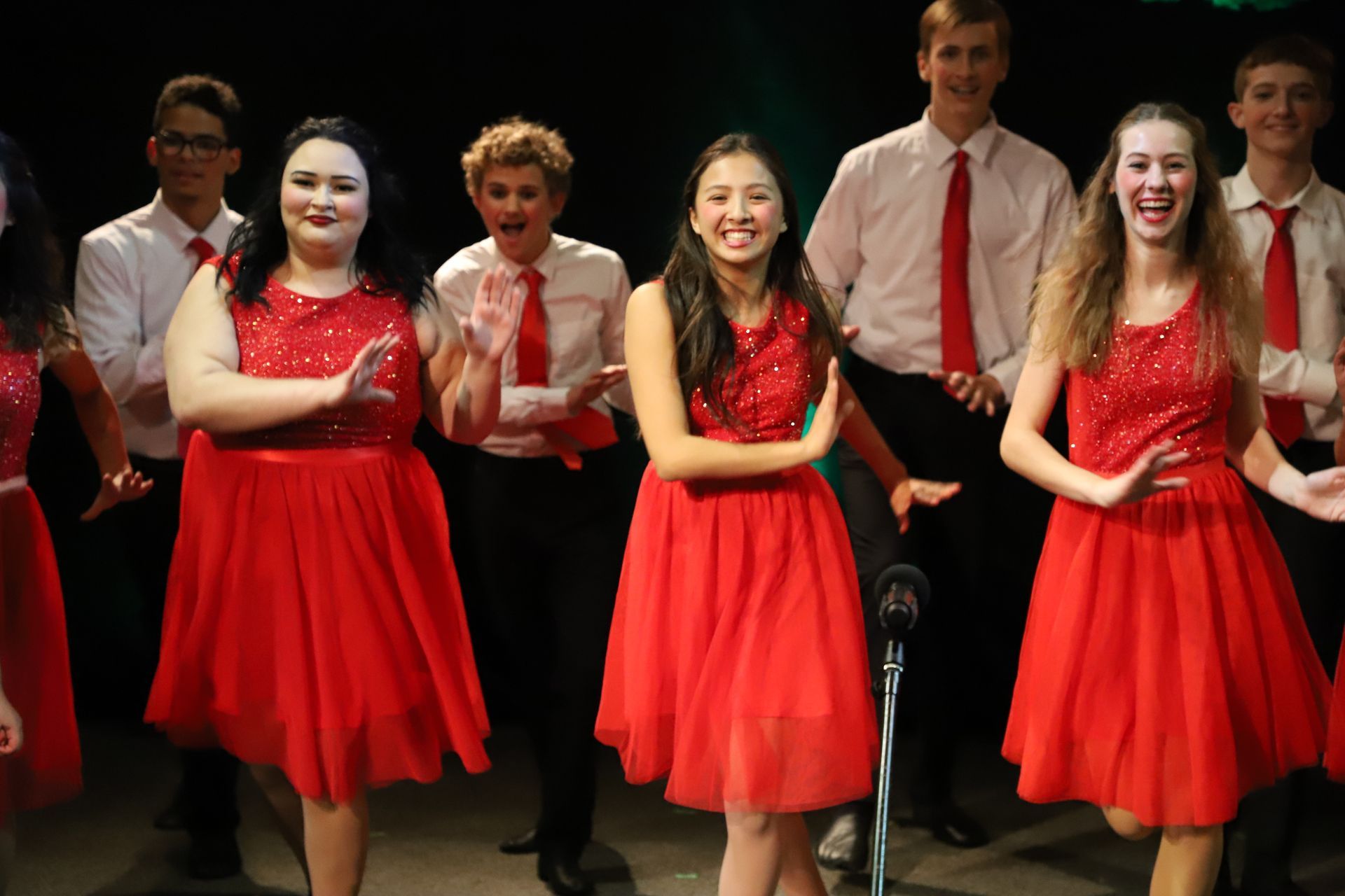 A group of people in red dresses are standing next to each other on a stage.