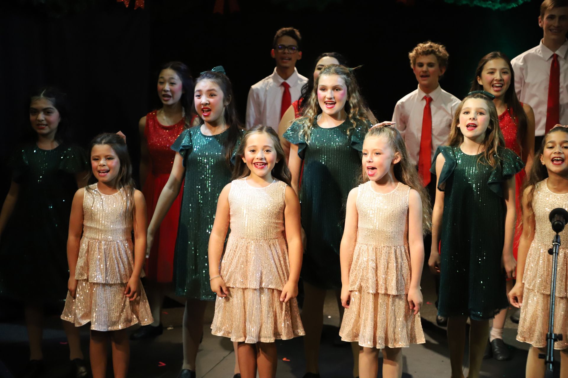 A group of young girls are singing in a choir on a stage.