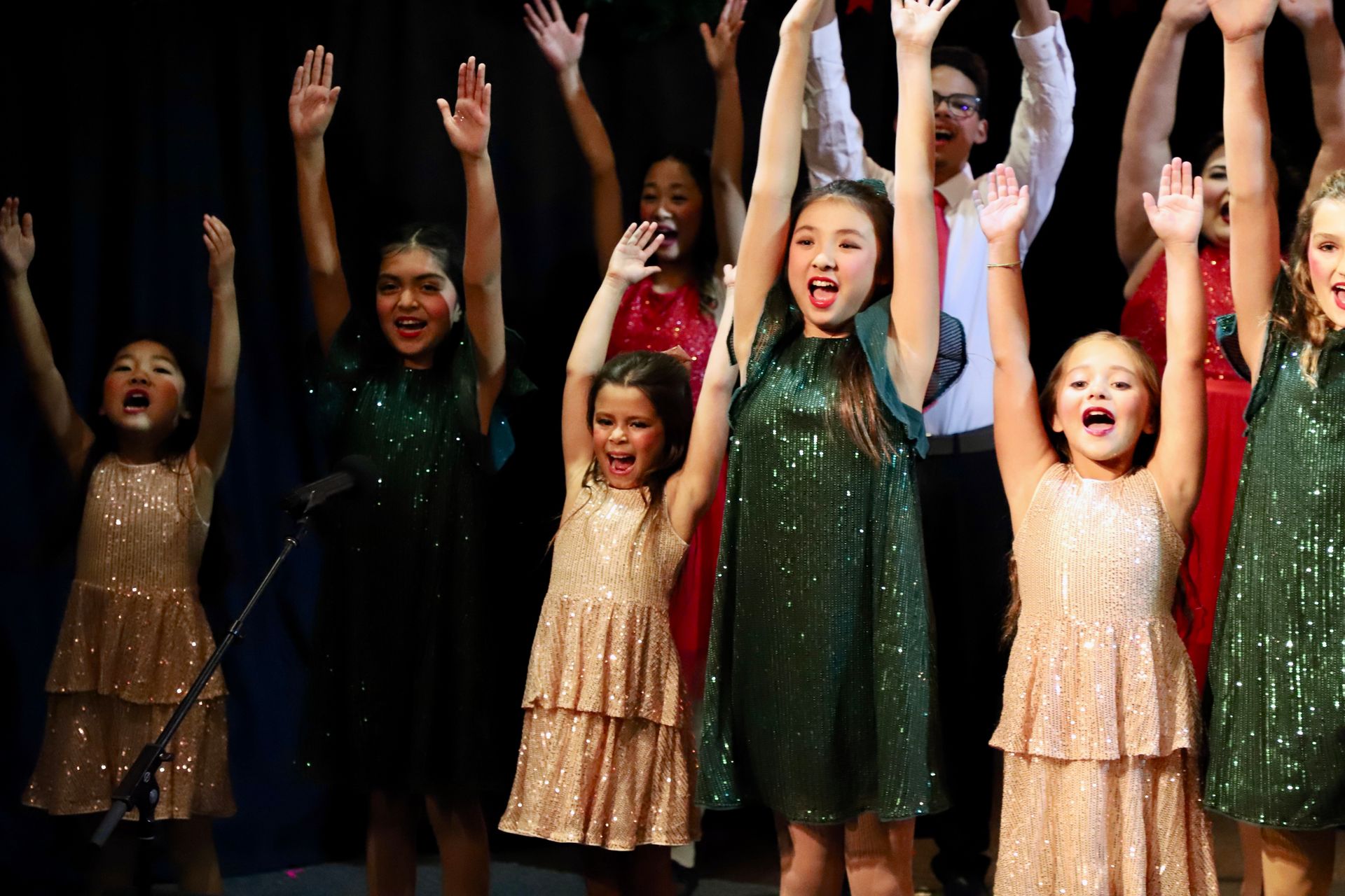 A group of young girls are standing on a stage with their hands in the air.