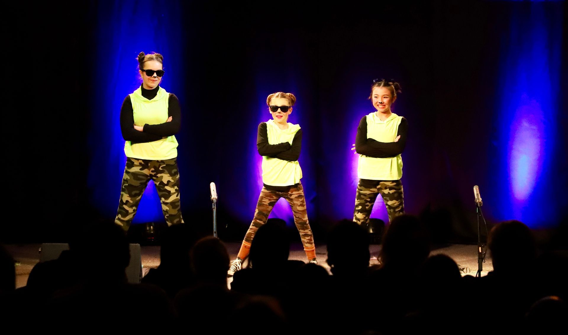 Three children are dancing on a stage in front of a crowd.