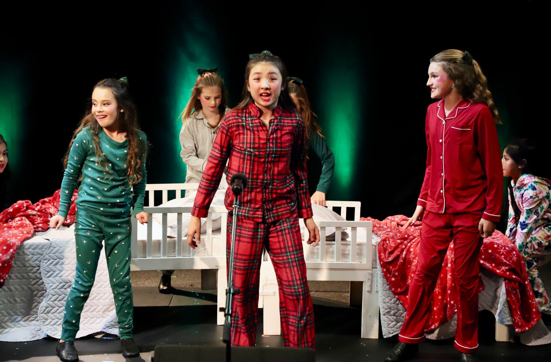 A group of young girls in pajamas are singing into a microphone on a stage.