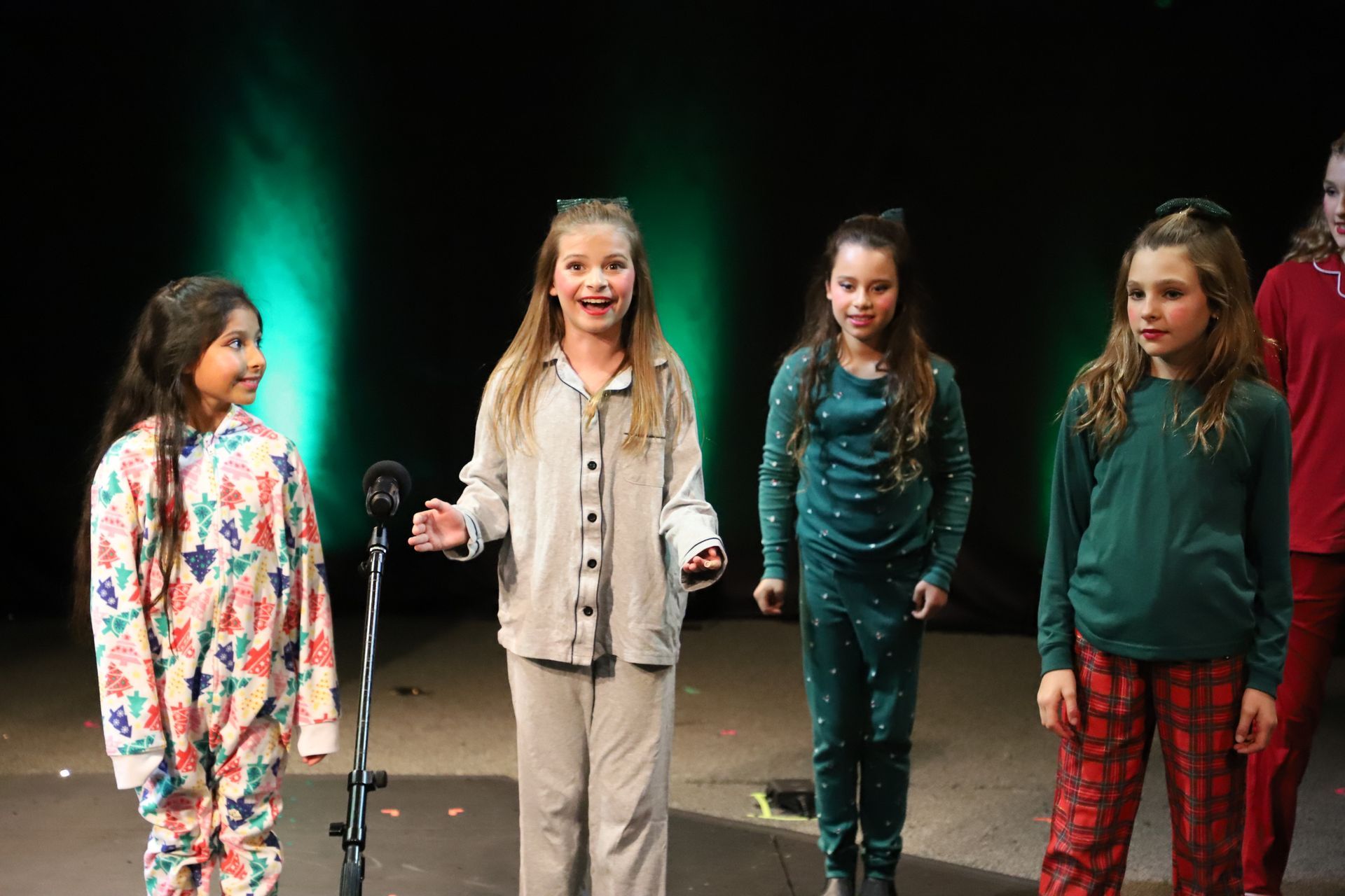 A group of young girls are standing in front of a microphone on a stage.