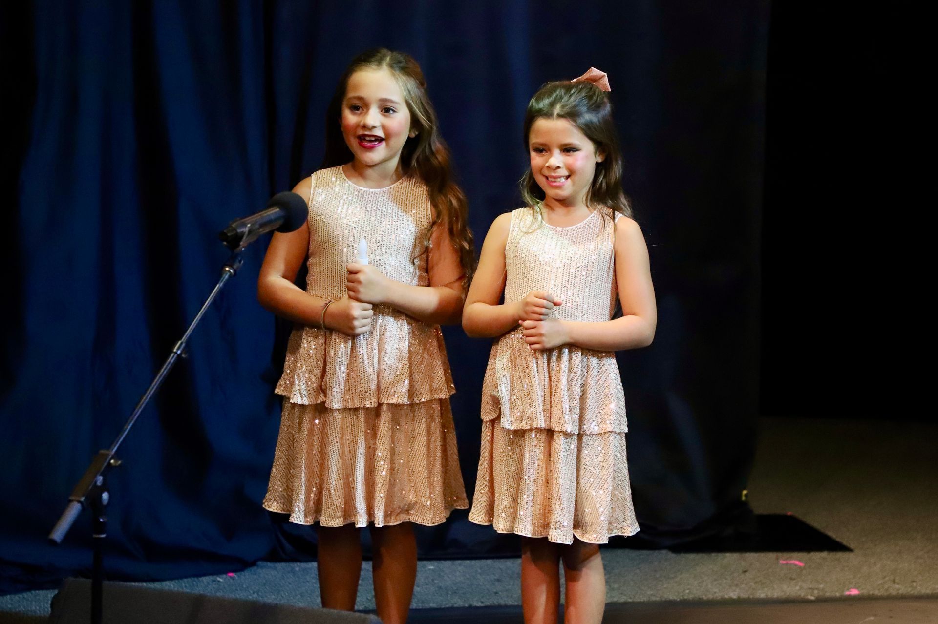 Two little girls are singing into microphones on a stage.