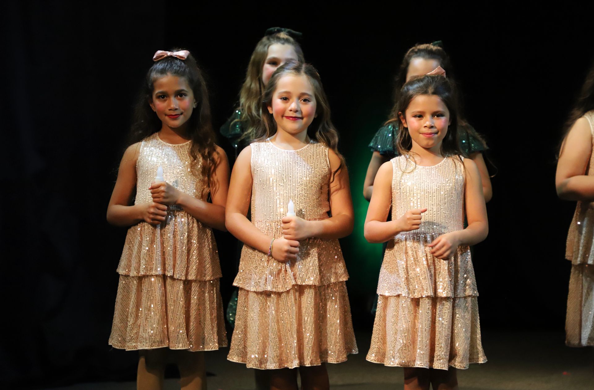 A group of young girls in sequined dresses are standing next to each other on a stage.