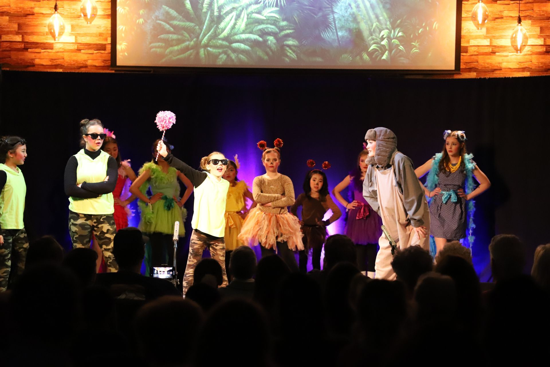 A group of children are standing on a stage in front of a crowd.