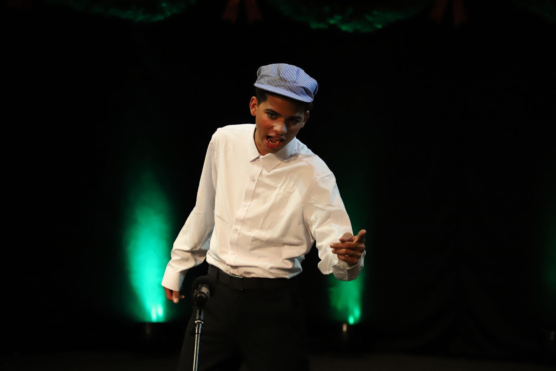 A young man wearing a hat is standing in front of a microphone on a stage.