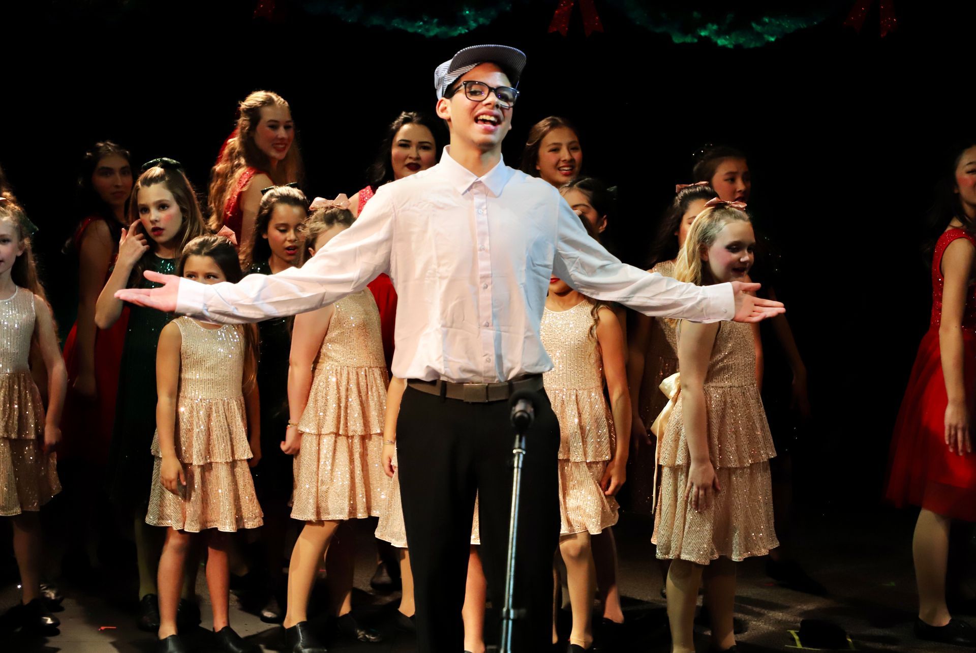 A man is standing in front of a microphone with his arms outstretched in front of a group of children.