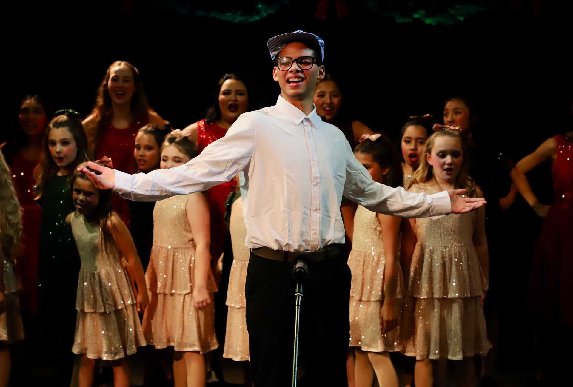 A man is standing in front of a microphone in front of a group of children.