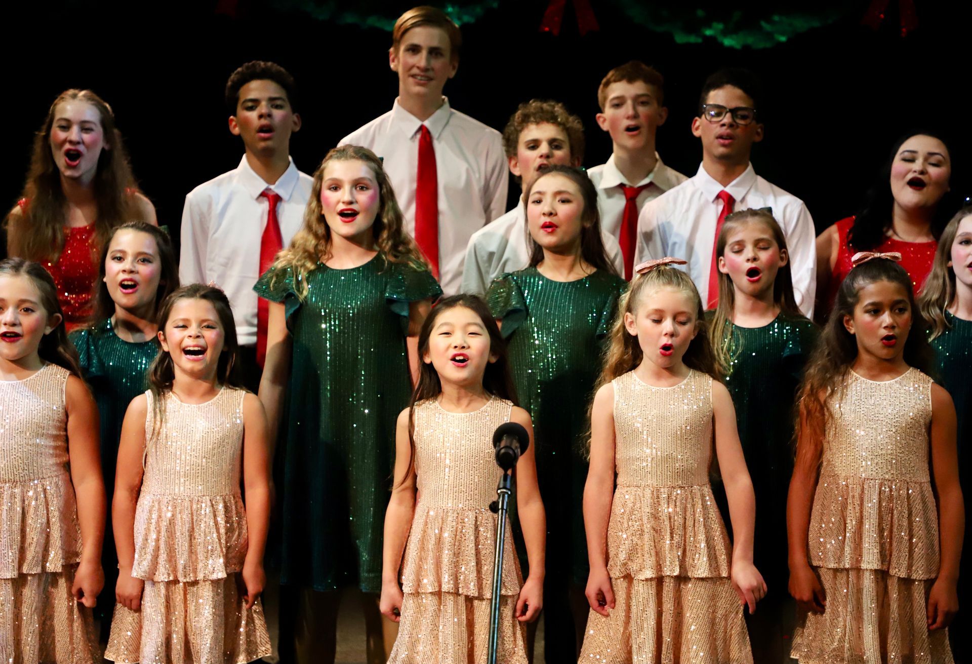 A large group of children are singing in a choir on a stage.