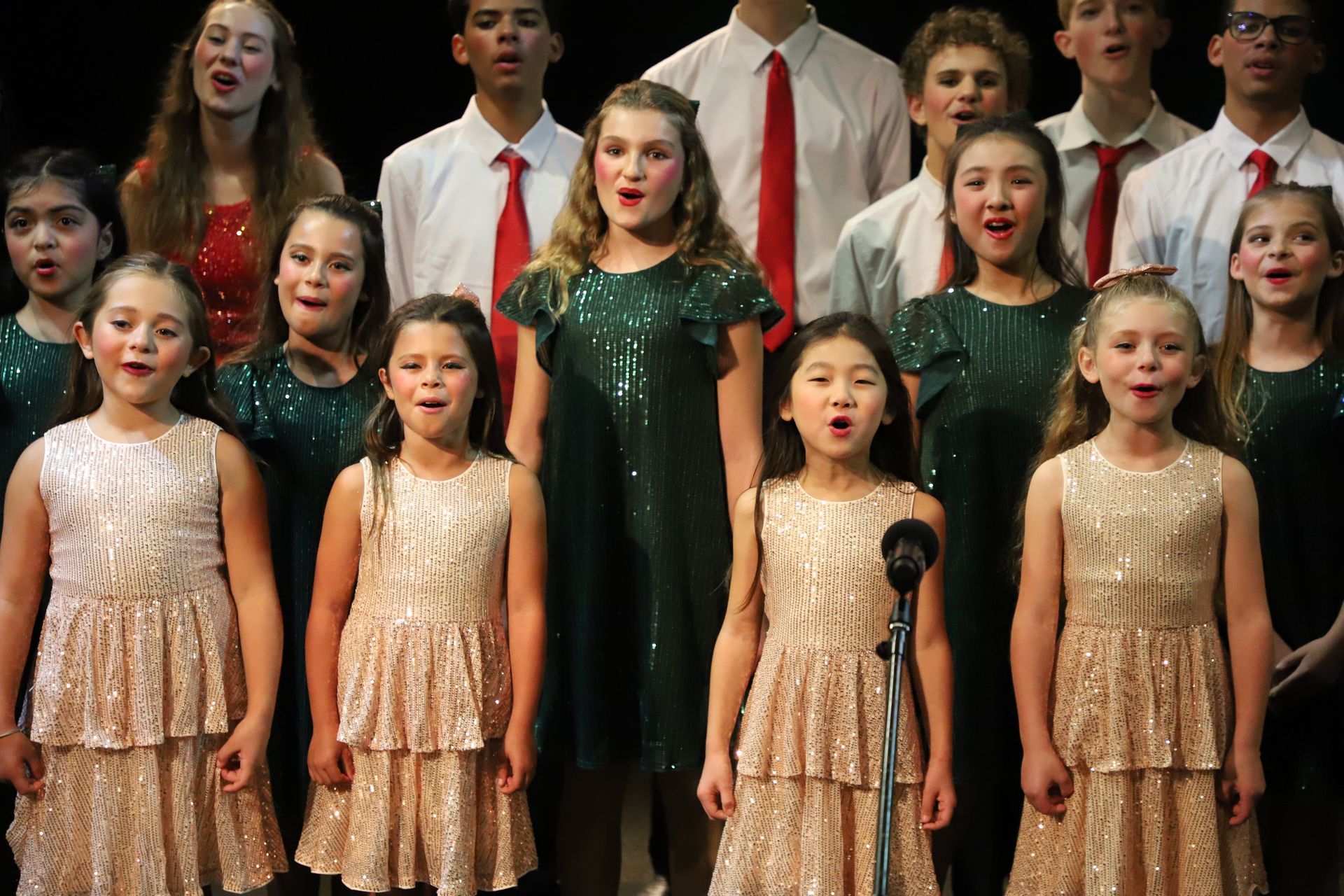 A group of children are singing in a choir on a stage.