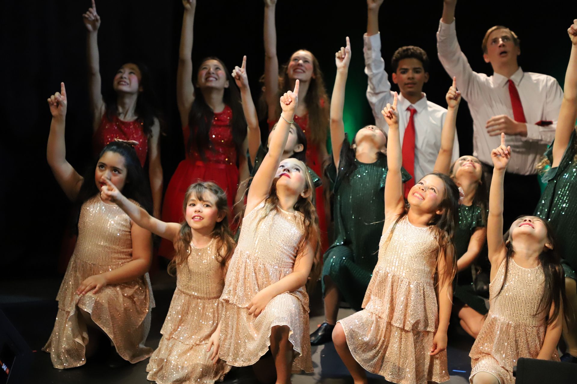 A group of children are dancing on a stage with their arms in the air.