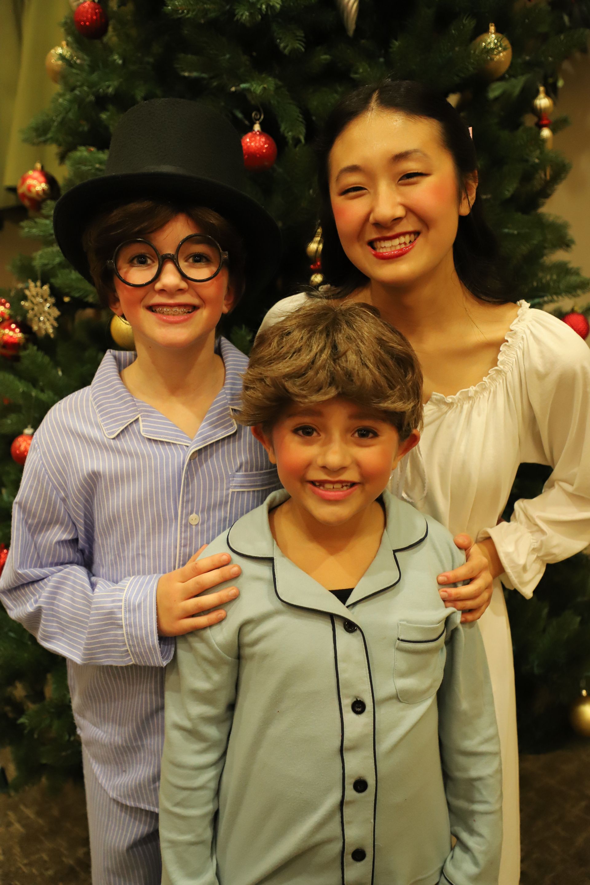 Three children are posing for a picture in front of a christmas tree.