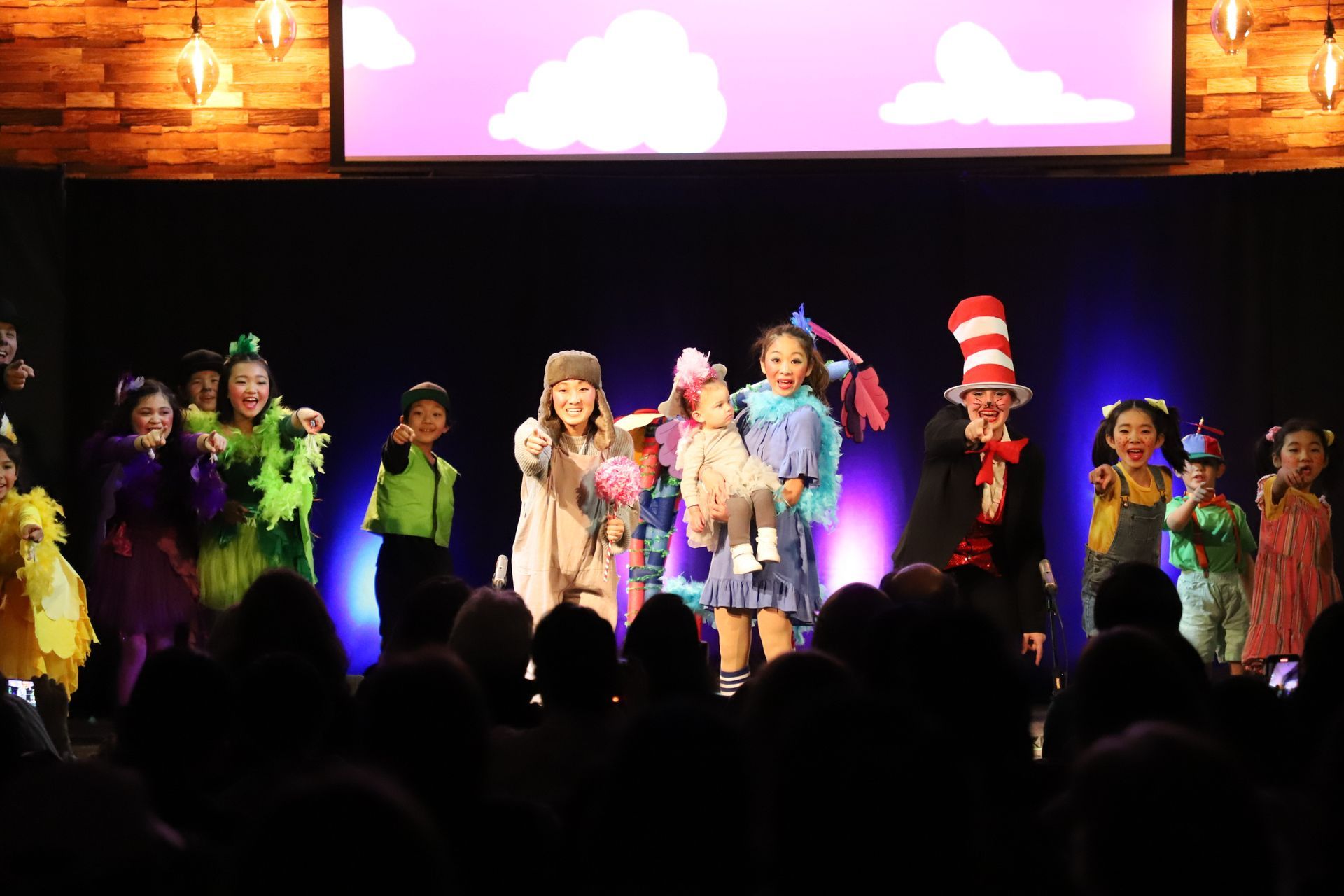 A group of children in costumes are standing on a stage in front of a crowd.