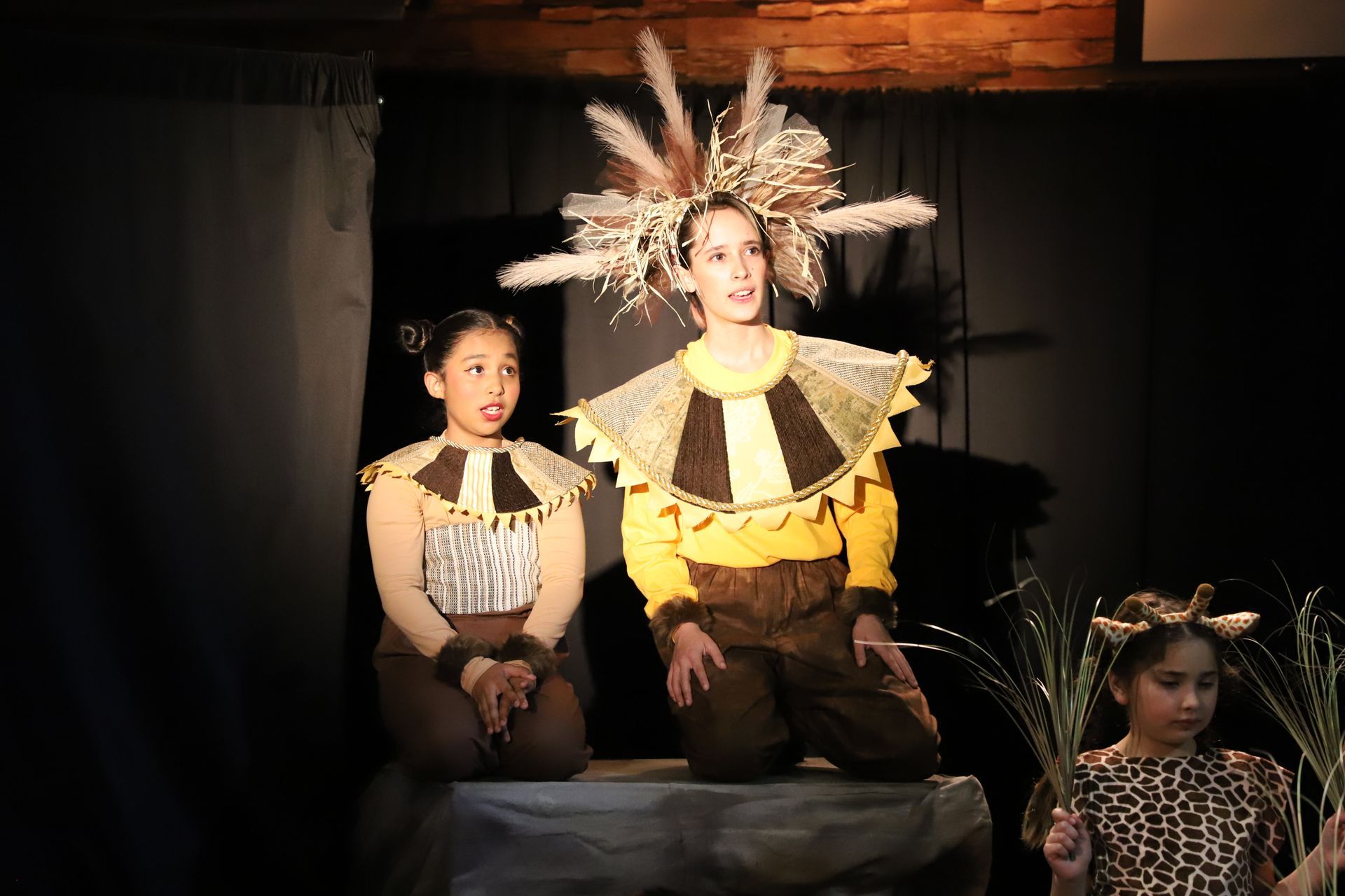 A group of children are sitting on a stage in costume.