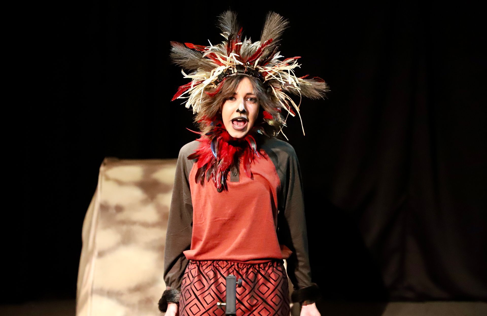 A woman is standing on a stage wearing a feathered headdress.