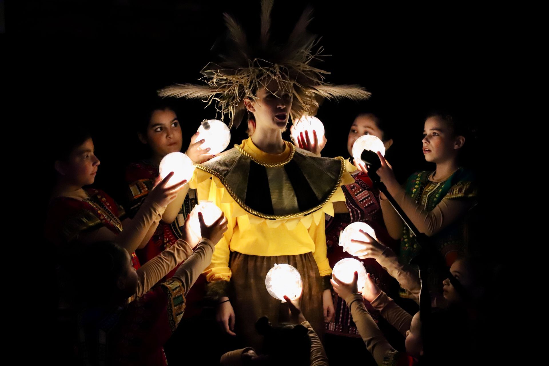 A group of people are holding light bulbs in their hands in a dark room.