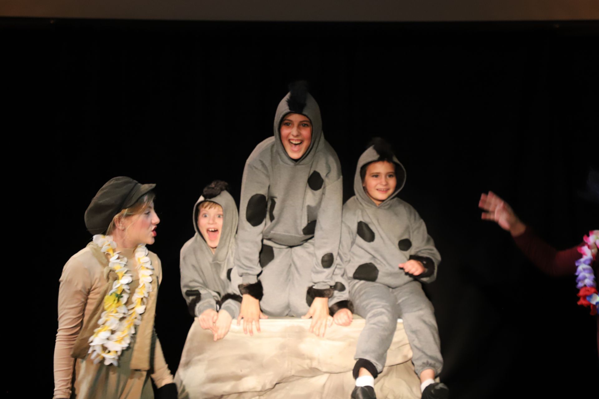 A group of children in costume are sitting on a rock on a stage.