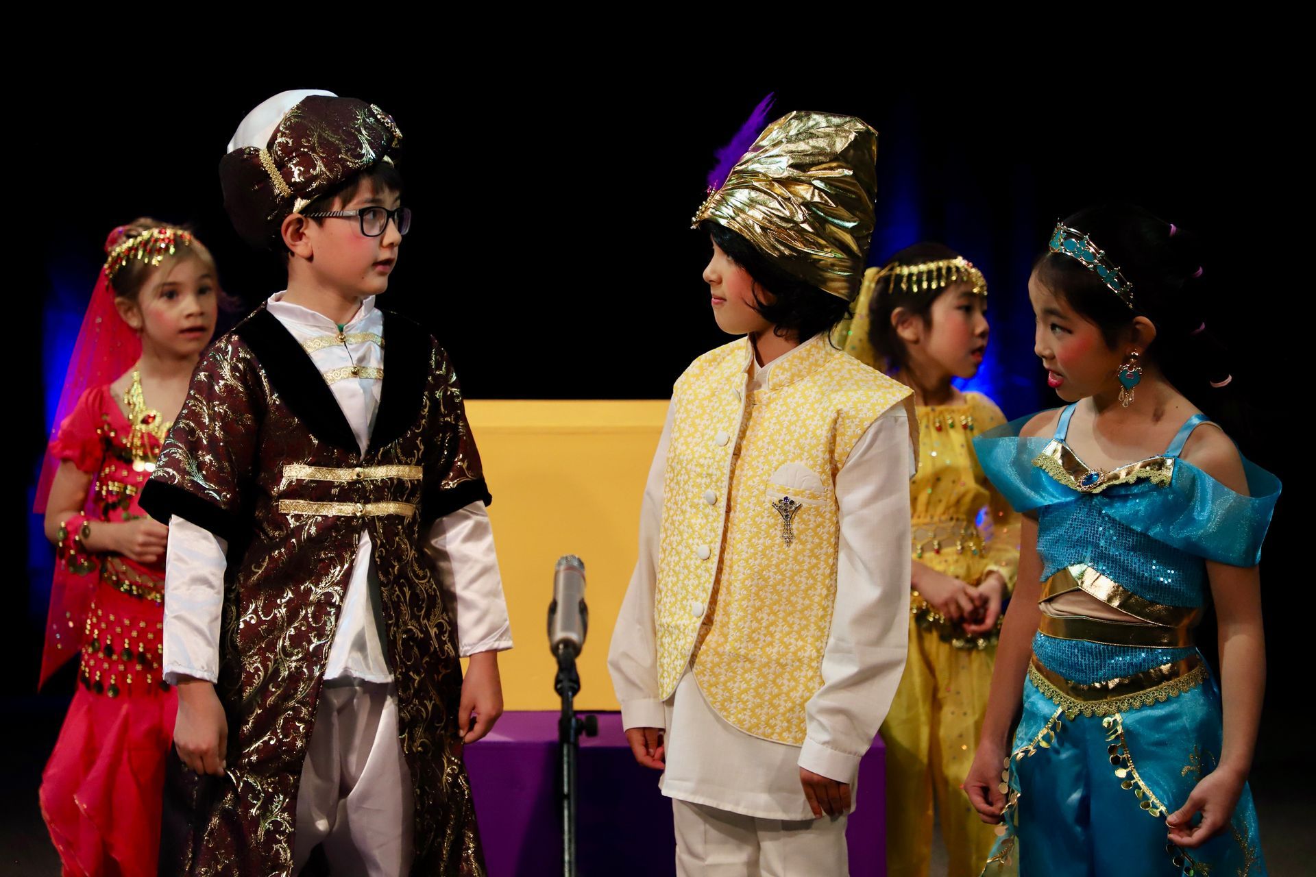 A group of children dressed in costumes are standing in front of a microphone