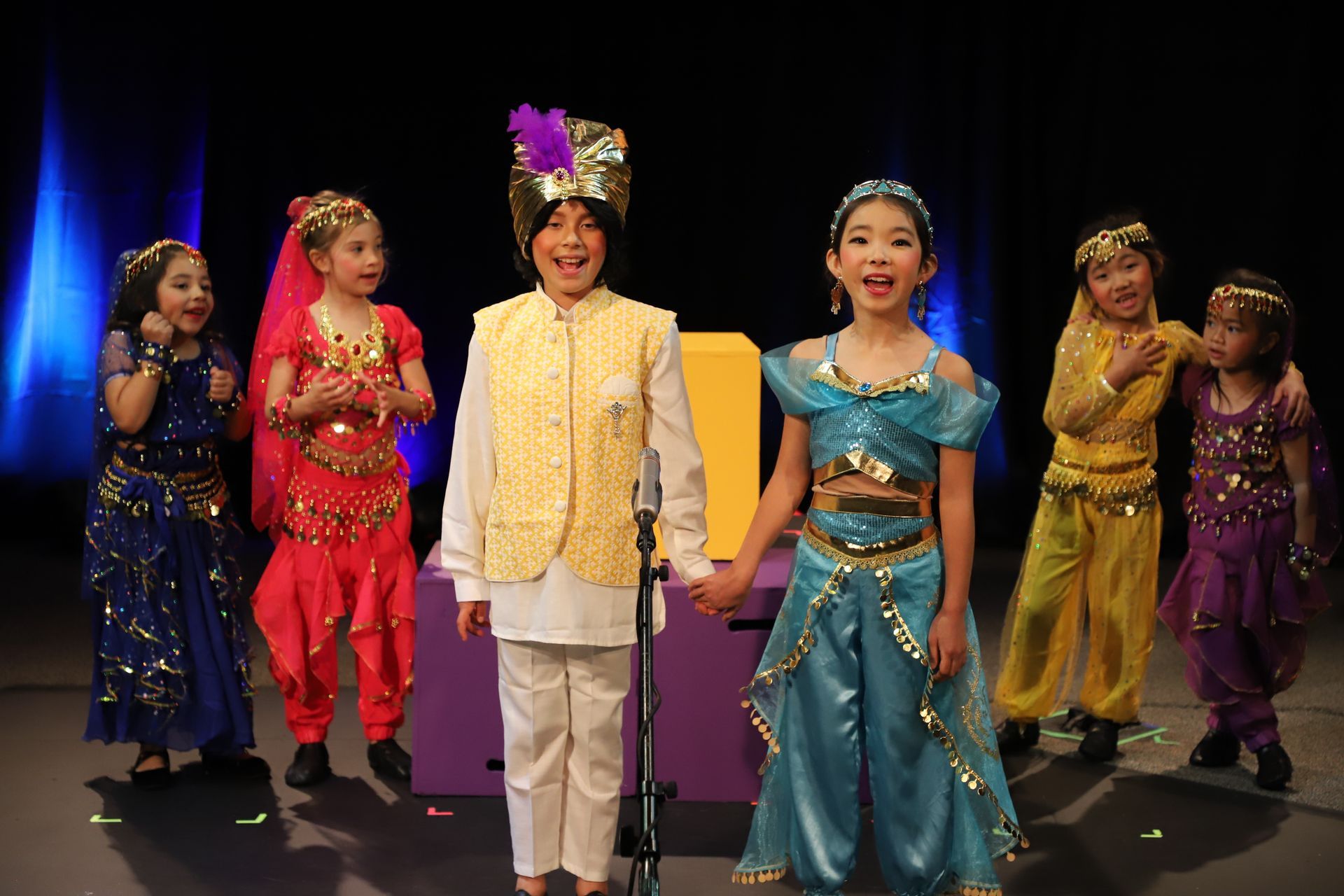 A group of children dressed in costumes are singing into a microphone on a stage.